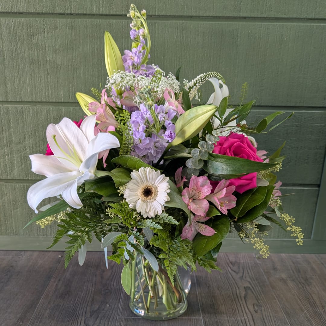 Mixed bouquet of lilies, roses, and daisies in a clear glass vase