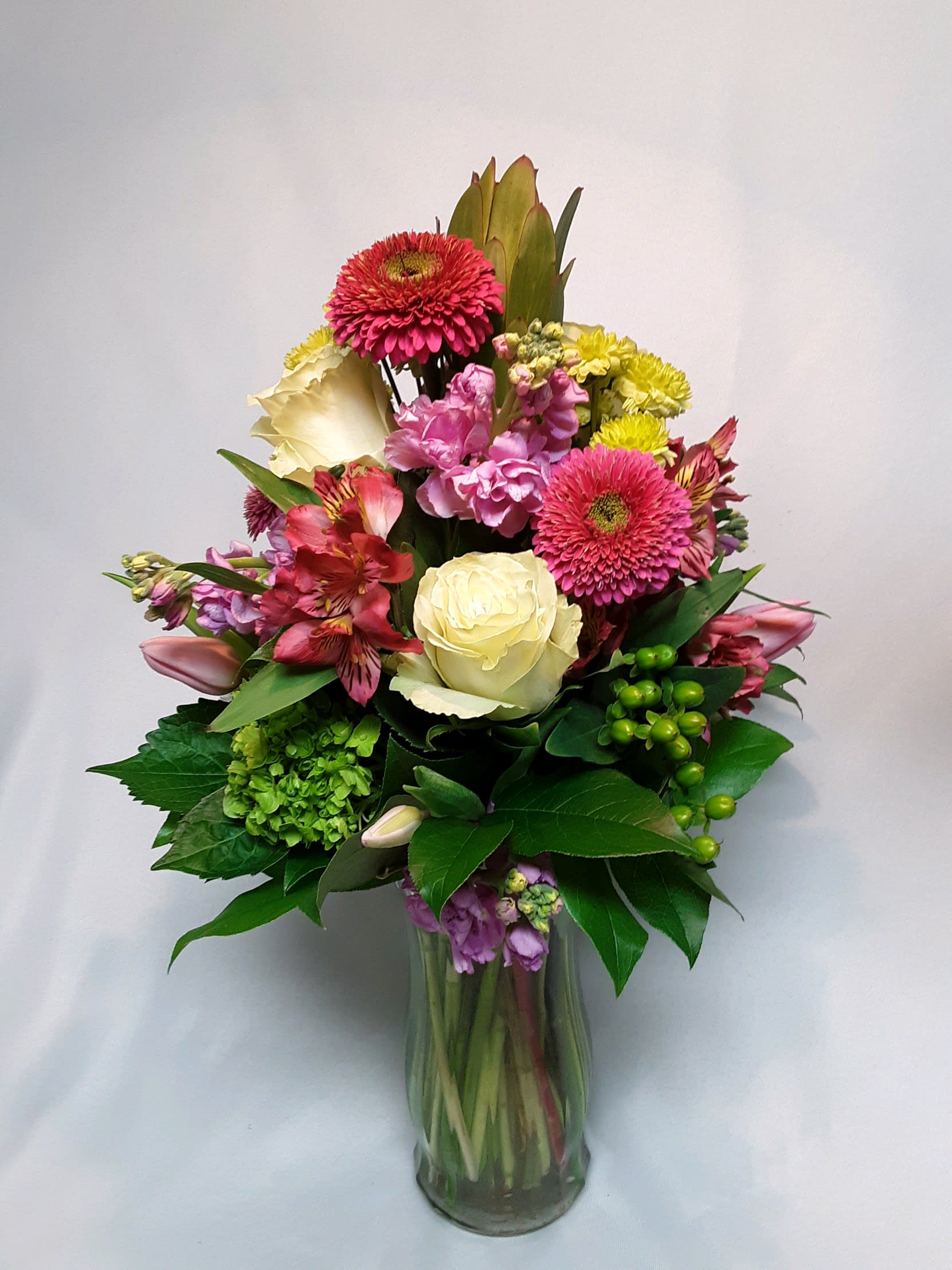 Mixed bouquet in a clear glass vase with pink, cream, and yellow flowers