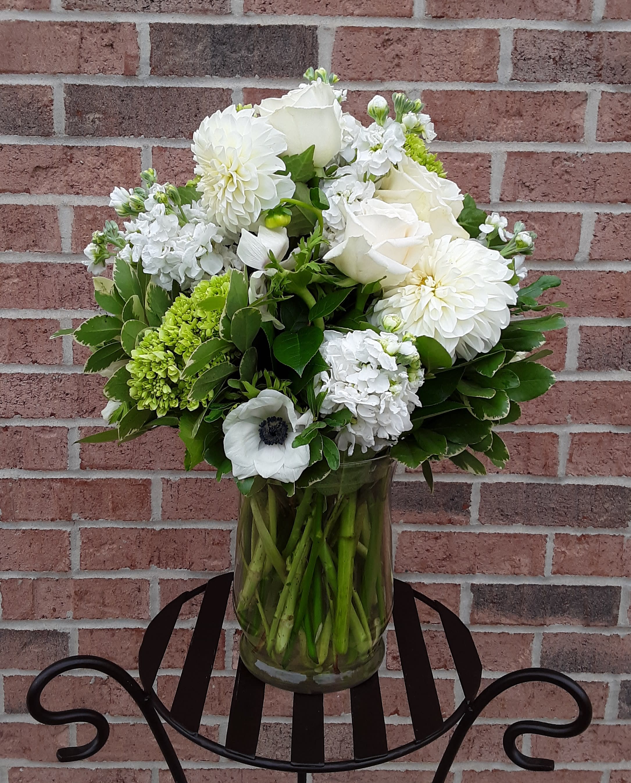 White floral arrangement in a glass vase with green accents