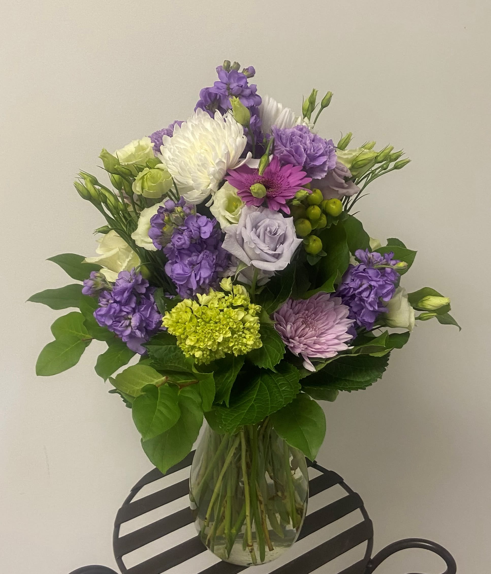 Bouquet of purple, white, and green flowers in a clear glass vase