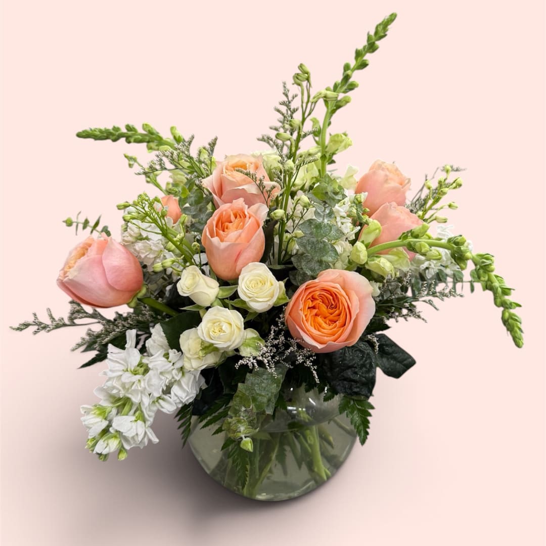 Peach and white roses arranged in a glass vase