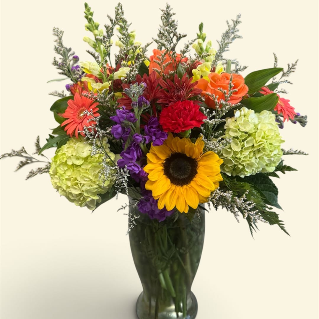 Colorful mixed bouquet in a tall glass vase with a sunflower and hydrangeas