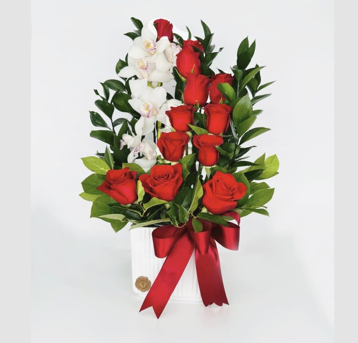 Red roses and white orchids arranged in a white vase with a red ribbon