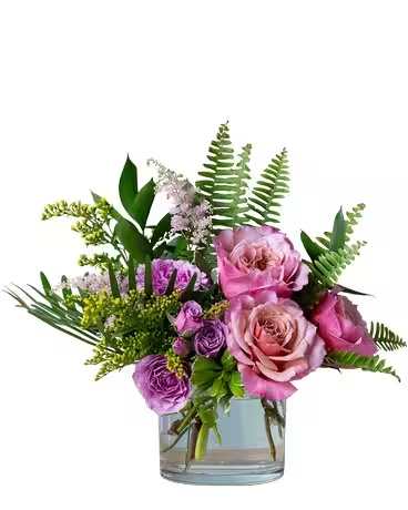 Pink and purple roses in a clear glass vase with fern foliage
