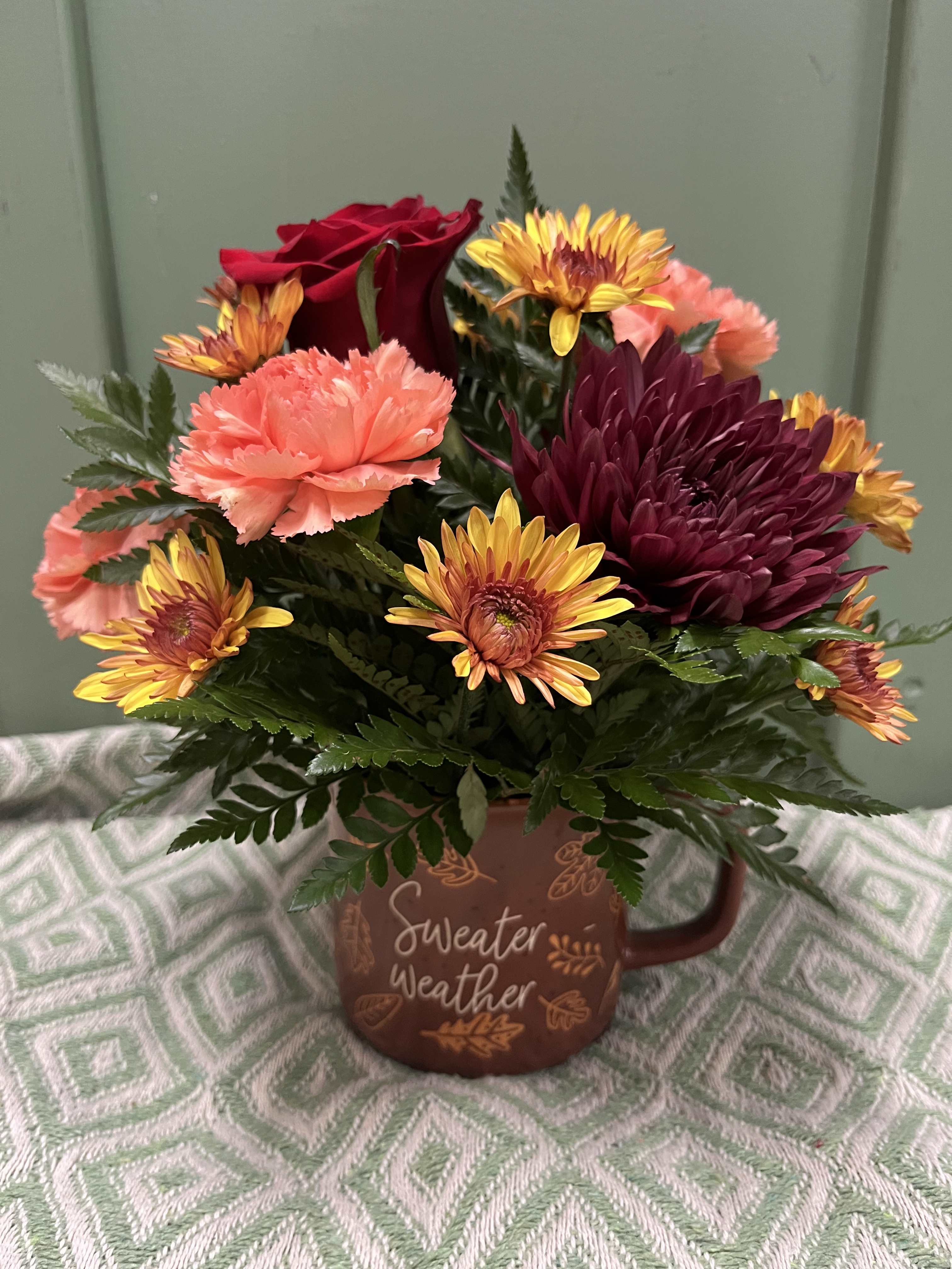 Bouquet of red roses, carnations, and chrysanthemums in a brown mug vase