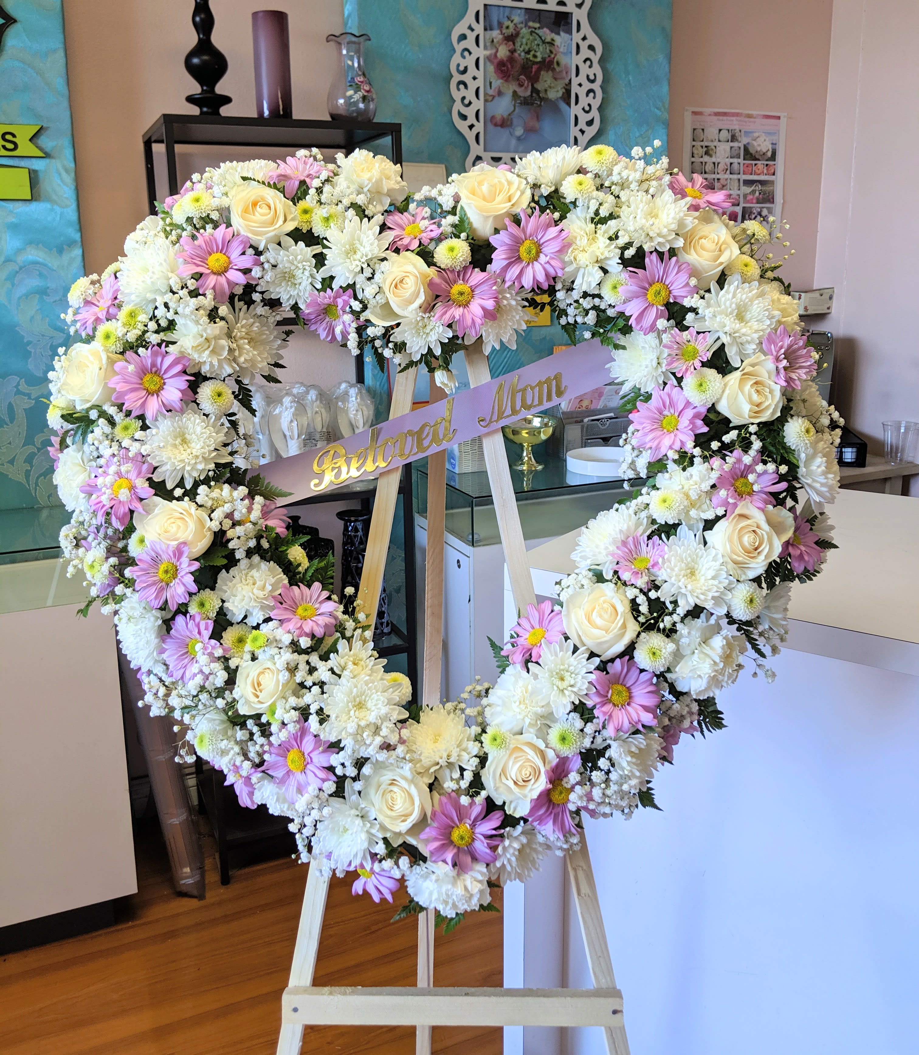 Heart-shaped floral wreath on an easel with a "Beloved Mom" ribbon