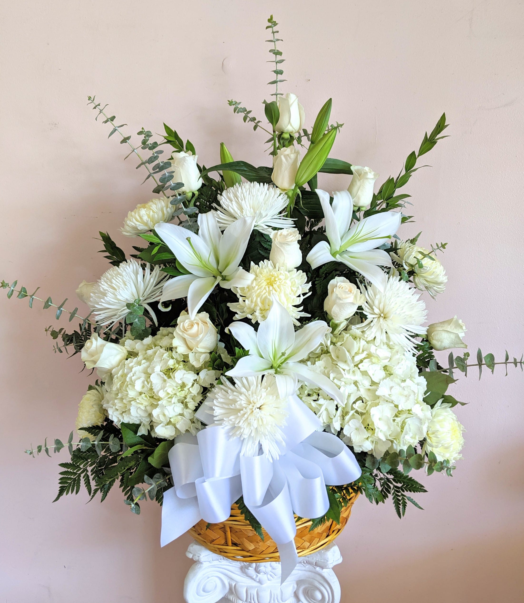 White floral arrangement in a woven basket with a large white ribbon