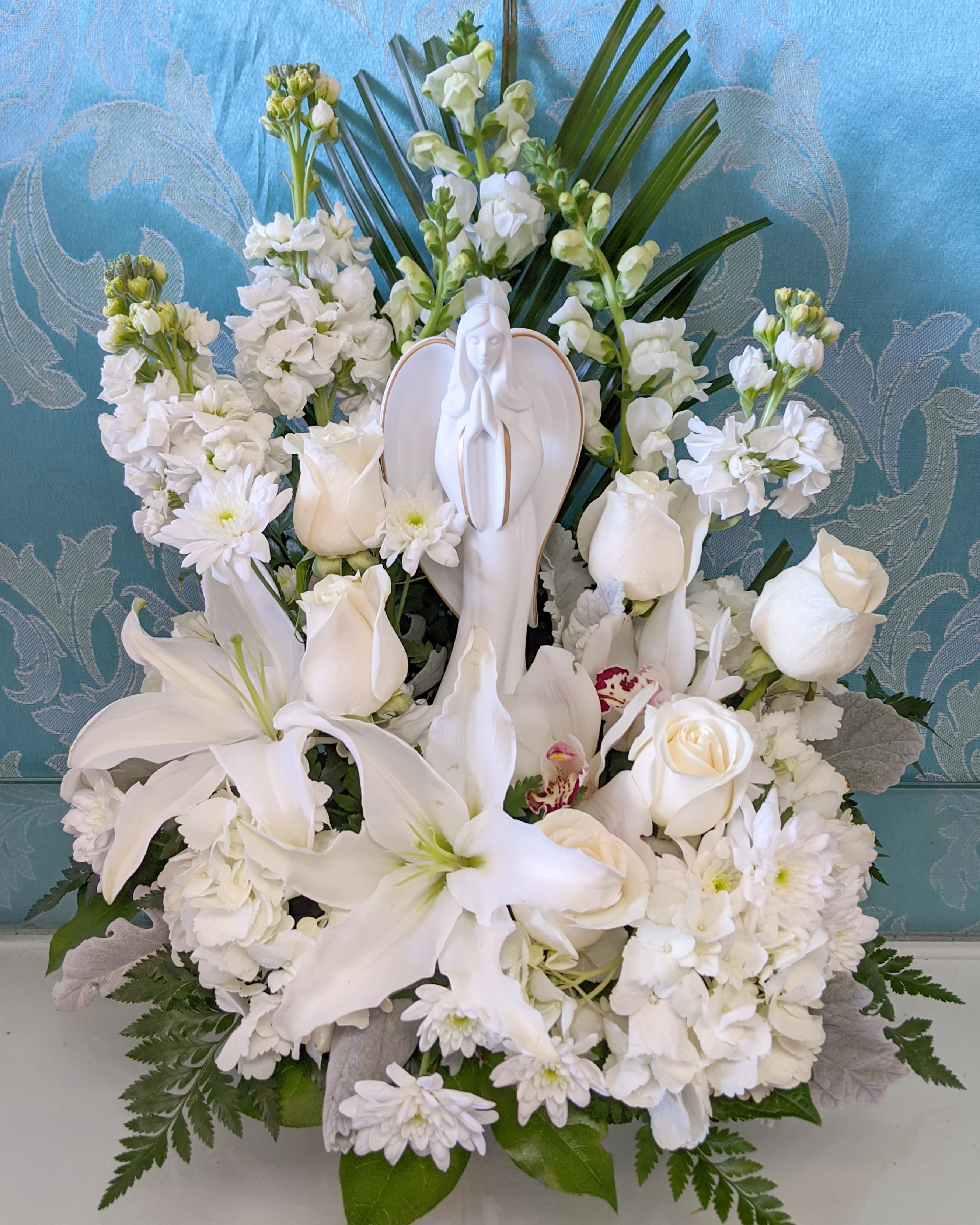 White floral sympathy arrangement with a praying angel figurine