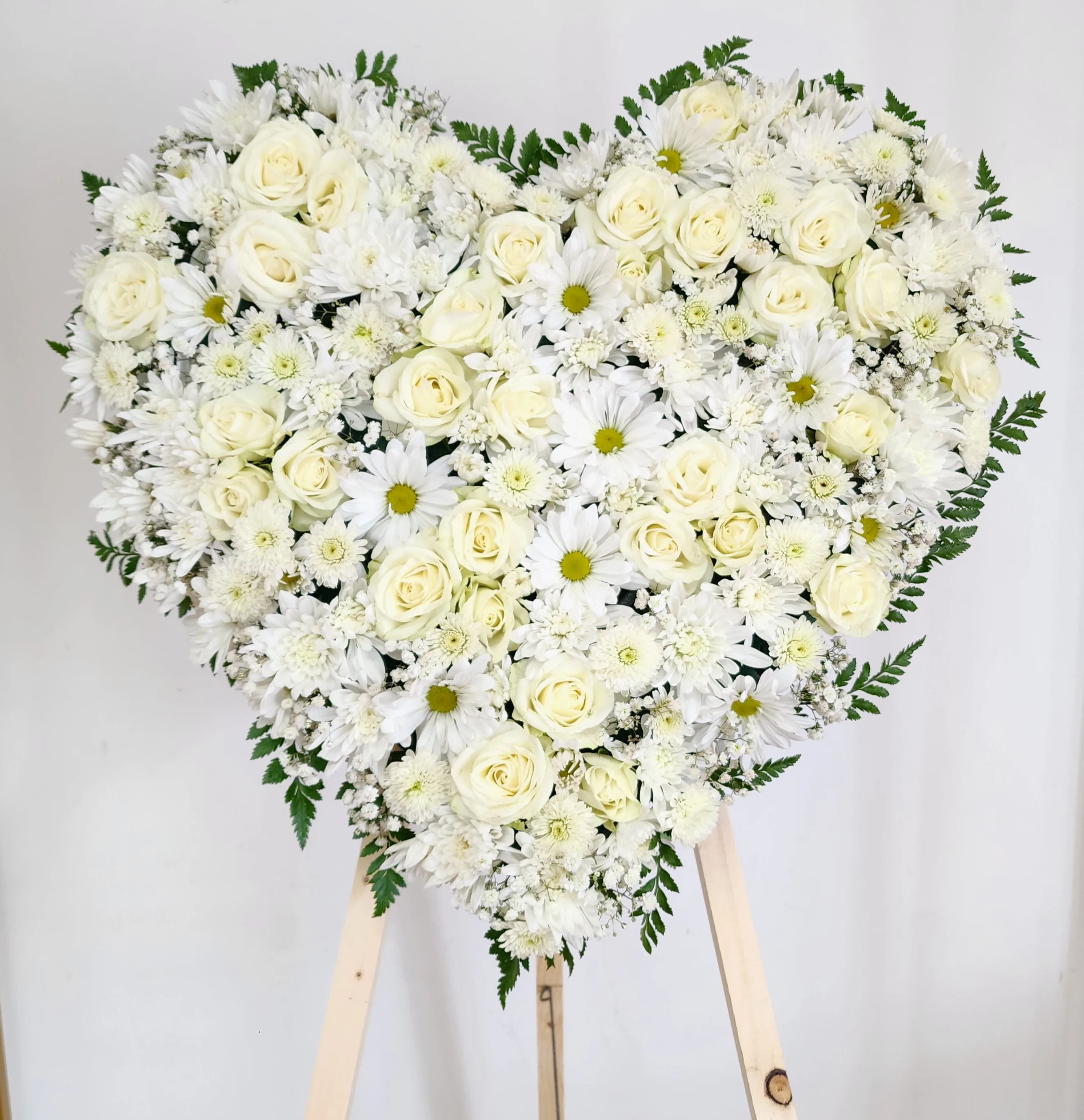 Heart-shaped arrangement of white roses and daisies on a stand