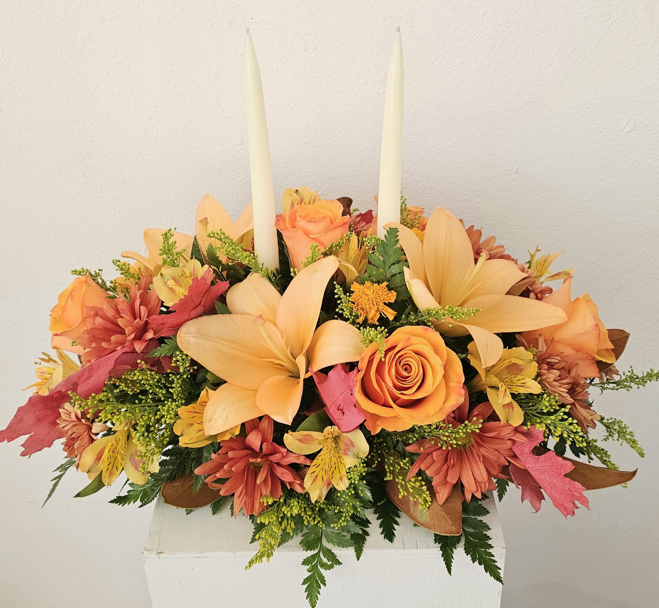 Orange and peach floral arrangement with two tall white taper candles