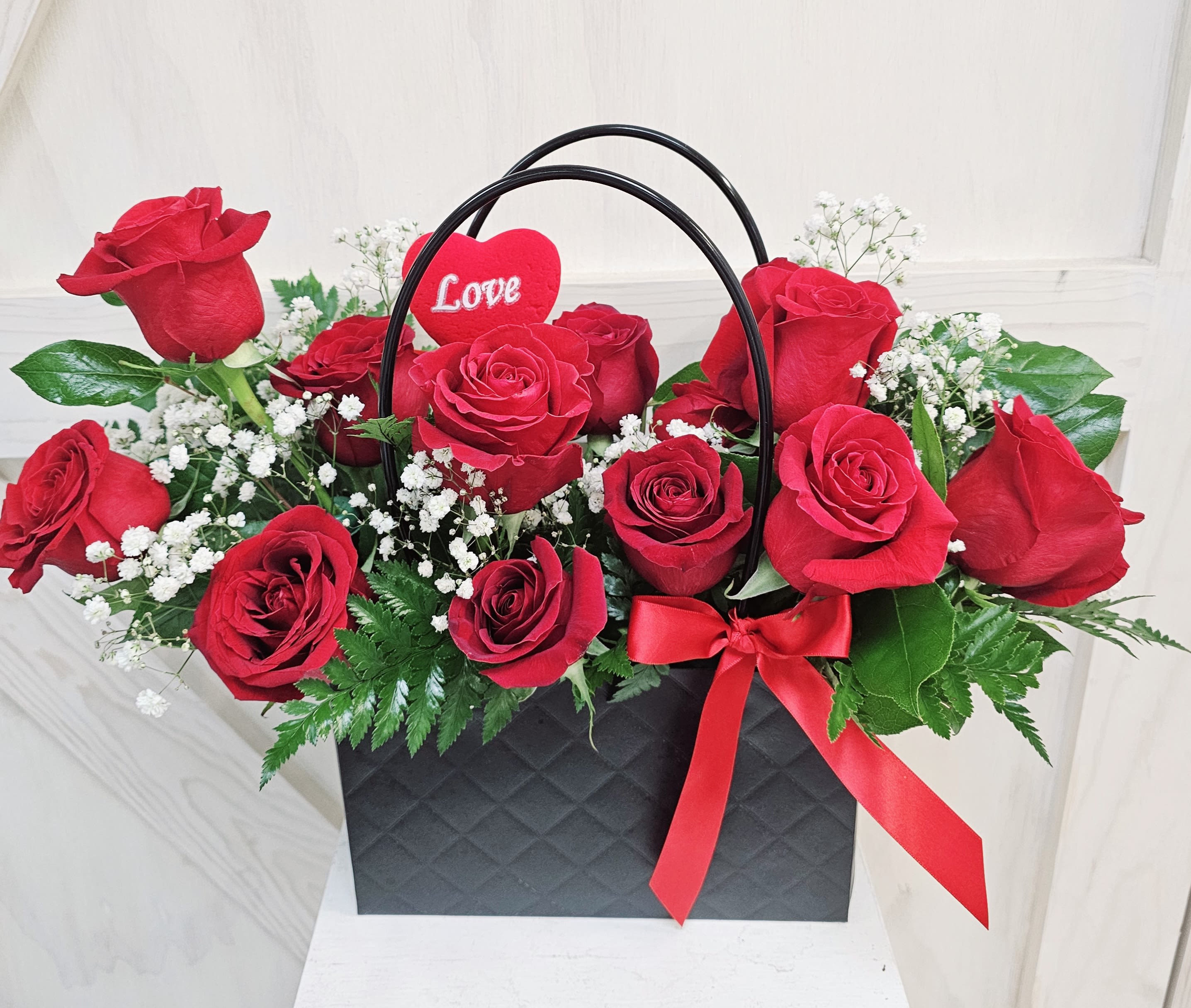 Red roses in a black gift bag with a red heart pick