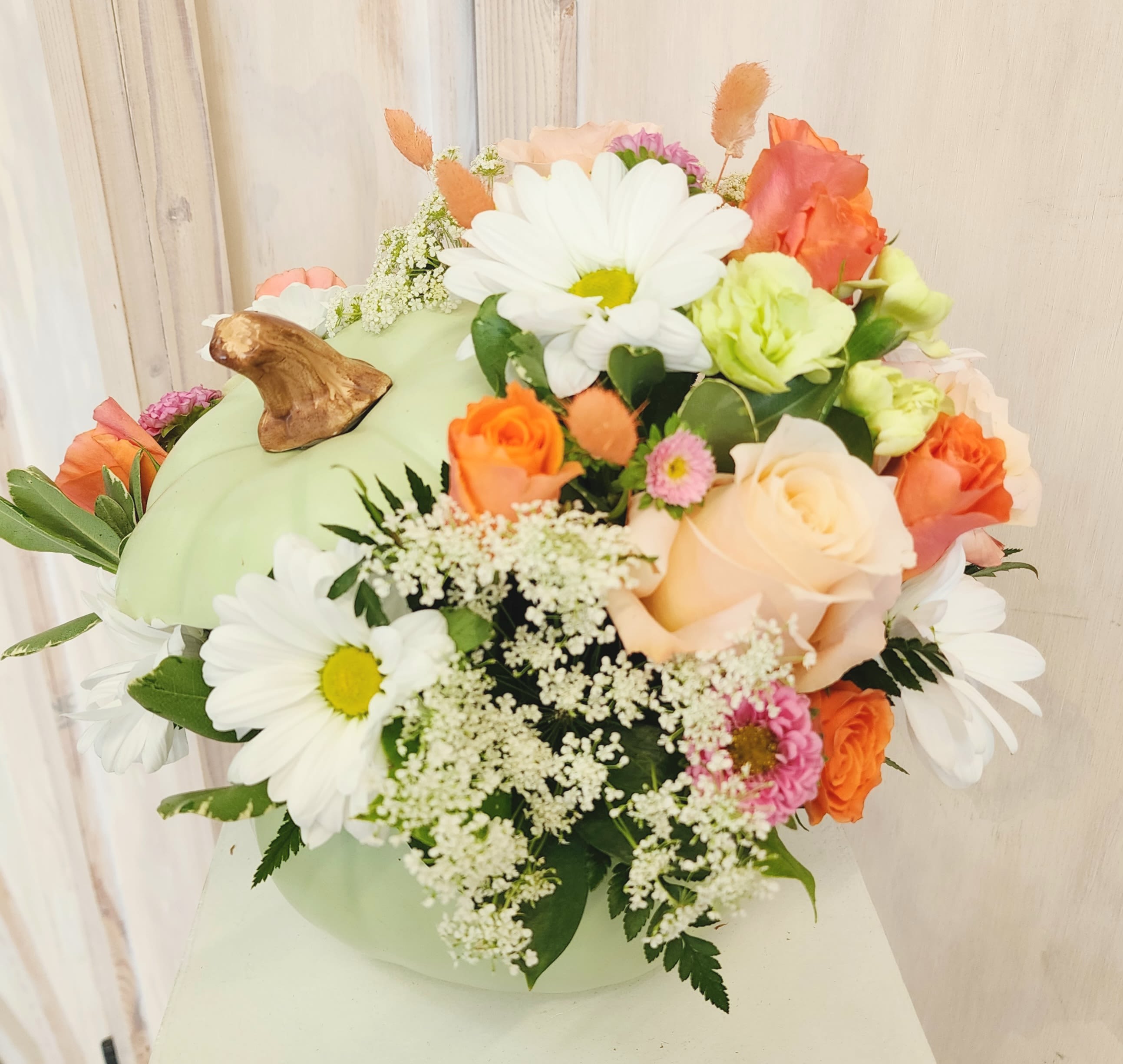 Mixed bouquet with daisies, roses, and small filler flowers in a pale green container