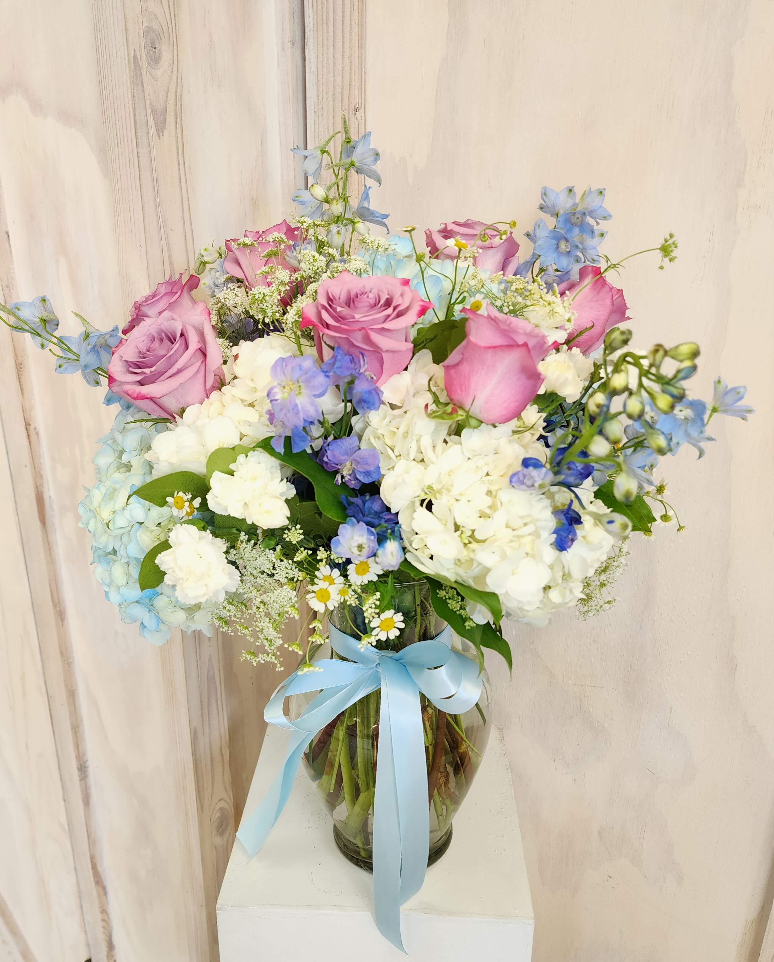 Pink roses and blue flowers in a glass vase with a blue ribbon