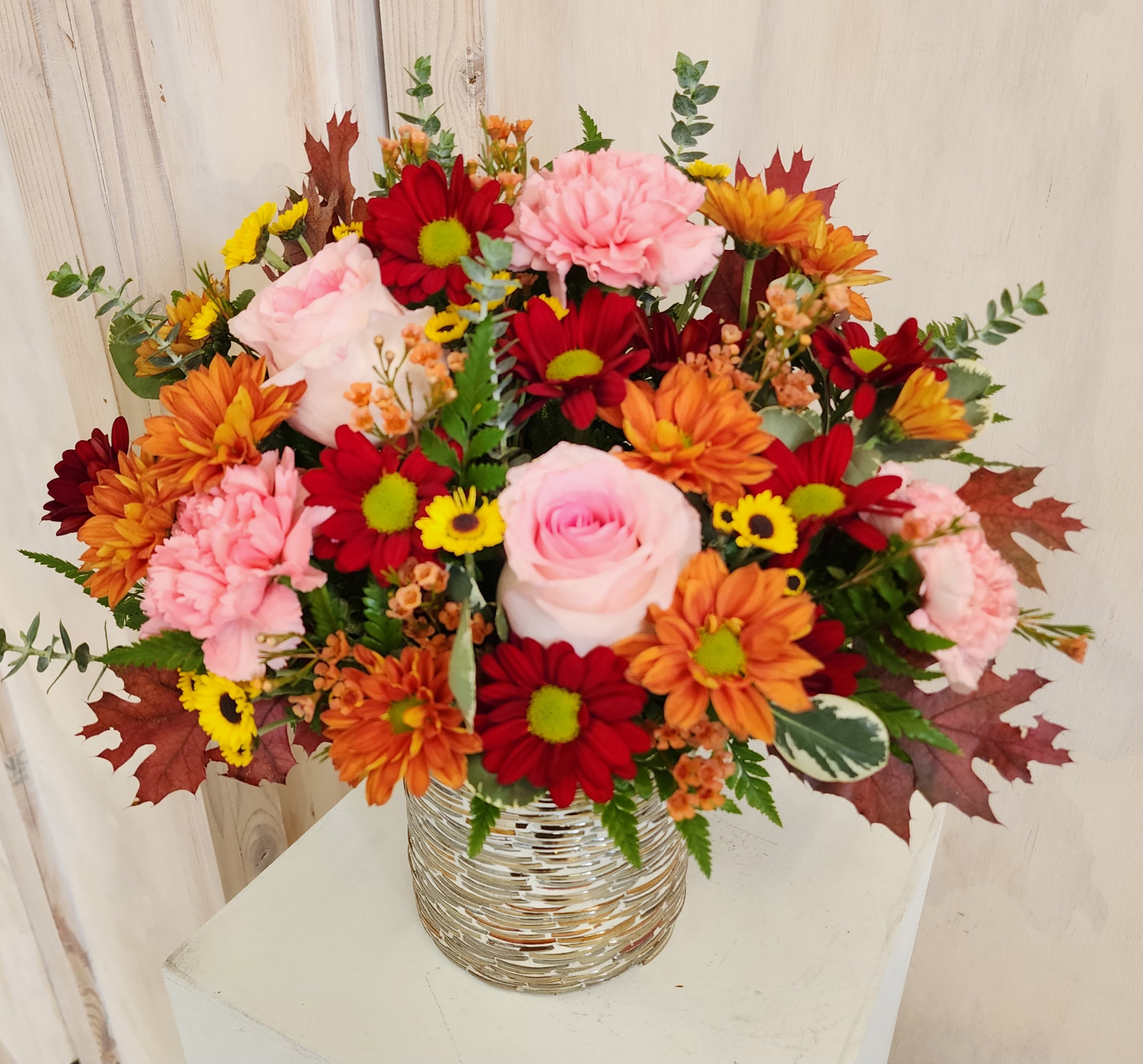 Mixed bouquet of pink, red, orange, and yellow flowers in a silver vase