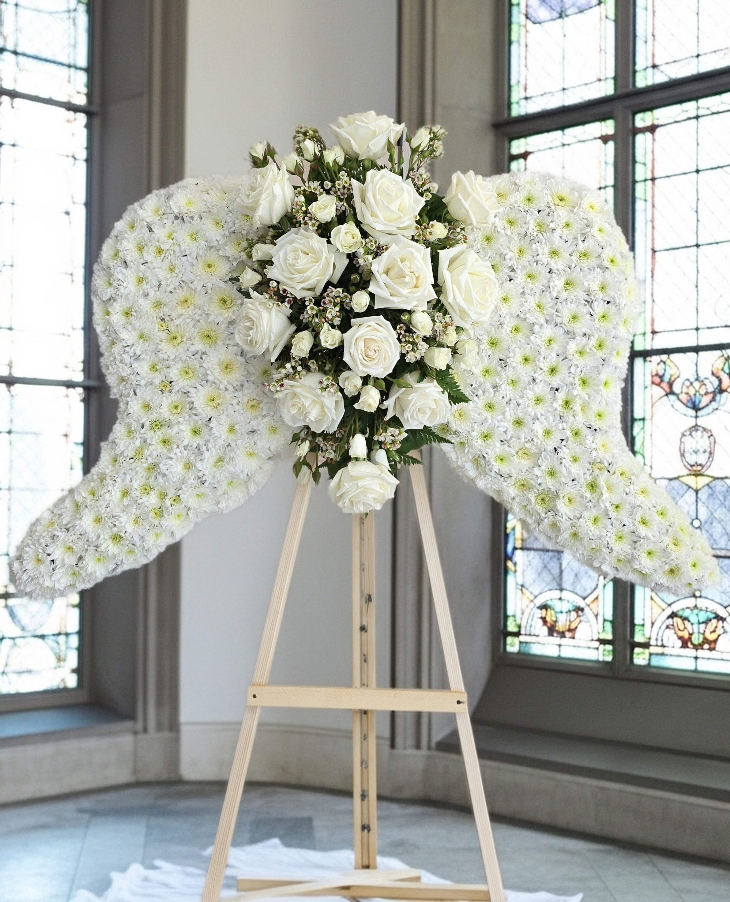 White floral angel wings on a wooden stand with roses in the center