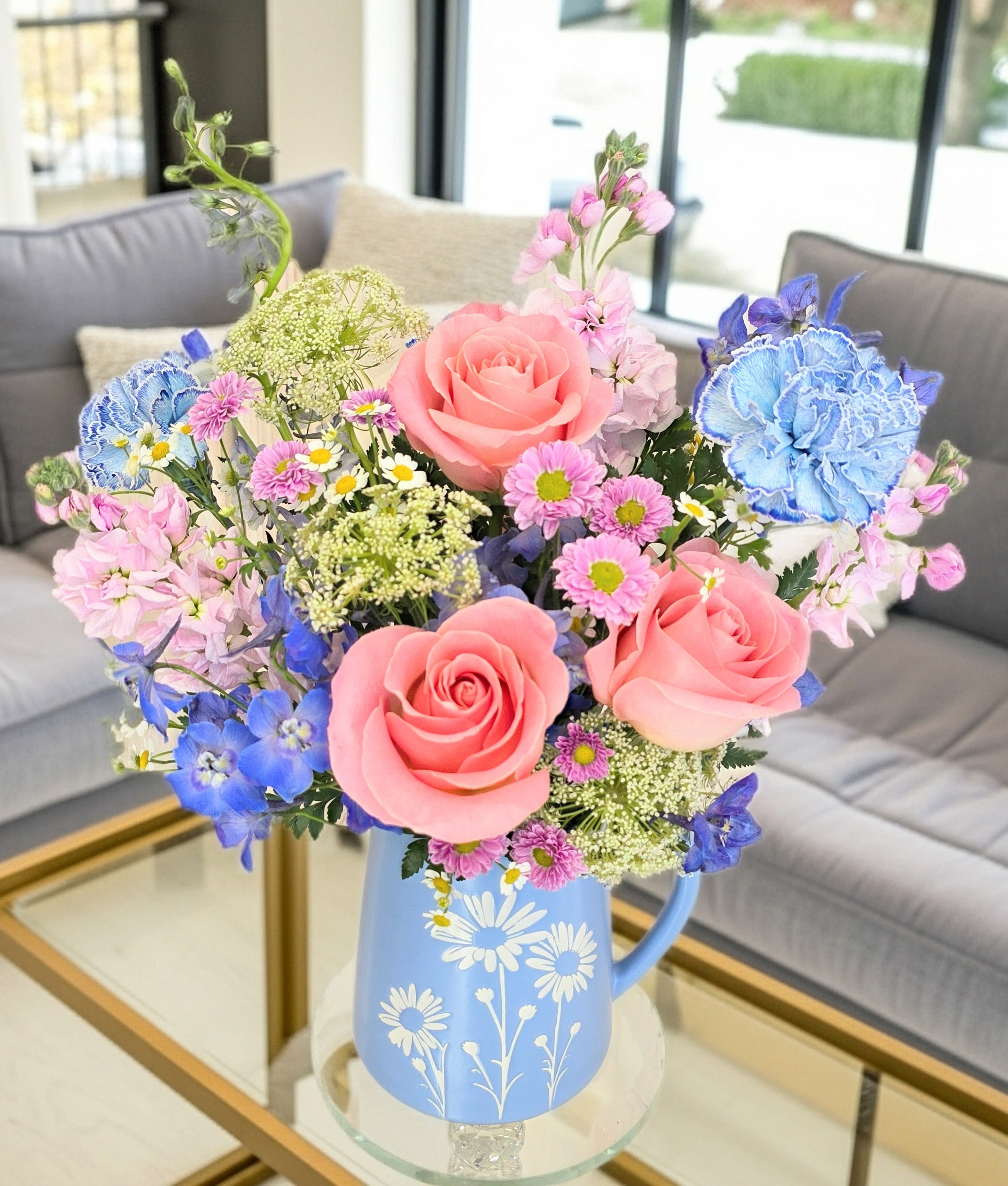 Periwinkle Blossoms - Periwinkle Blossoms greets them with a playful burst of color-pink roses and pink stargazer lilies sit at the heart of this flower arrangement, accented by vivid blue carnations and small white daisy-like fillers for a fresh, springtime look. Designed as a birthday bouquet, thank-you gift, or cheerful centerpiece for a spring celebration, the mix of pastel and saturated hues creates a lively, slightly romantic impression that will make the person you're thinking of feel seen and celebrated.