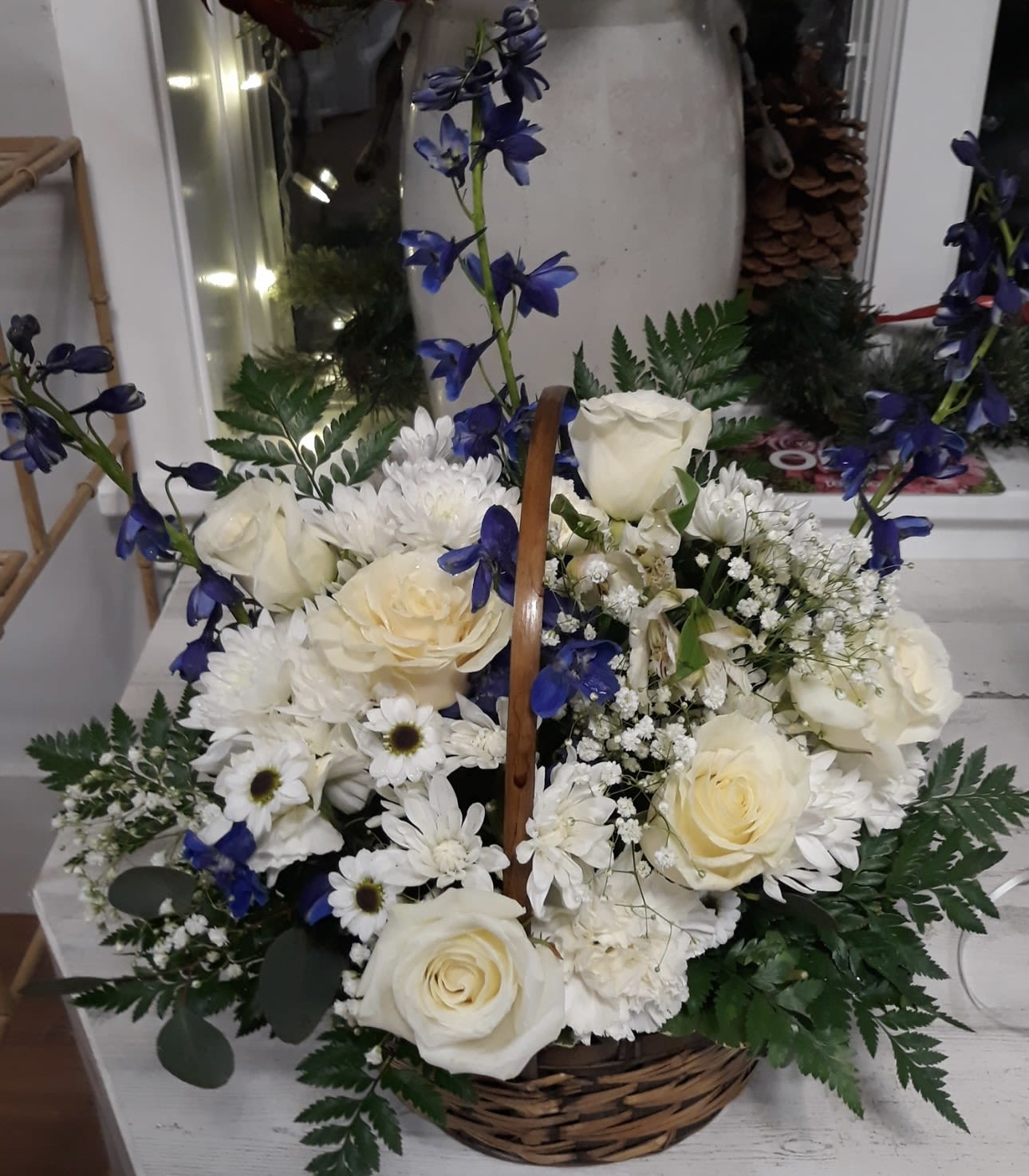 Basket arrangement of white roses and daisies with blue delphinium accents and ferns