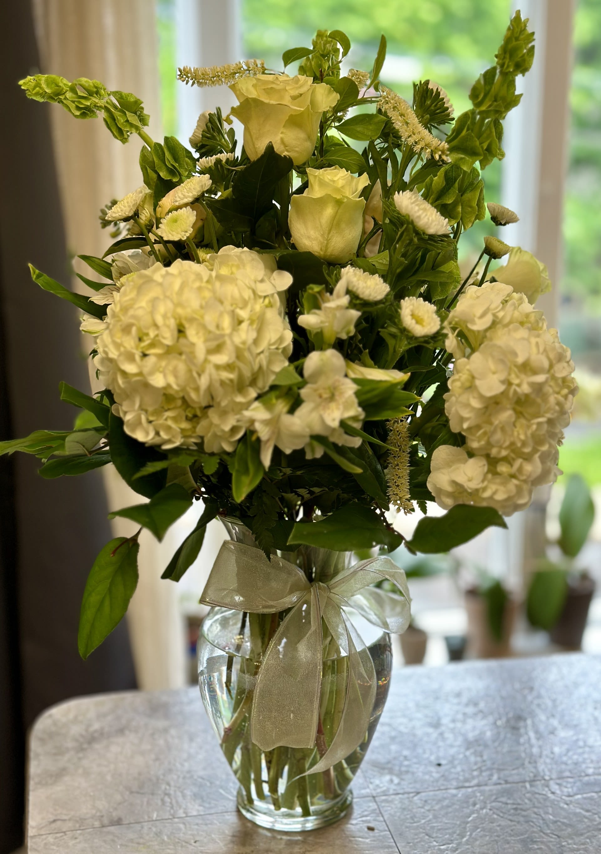 White floral arrangement in a clear glass vase with a ribbon bow