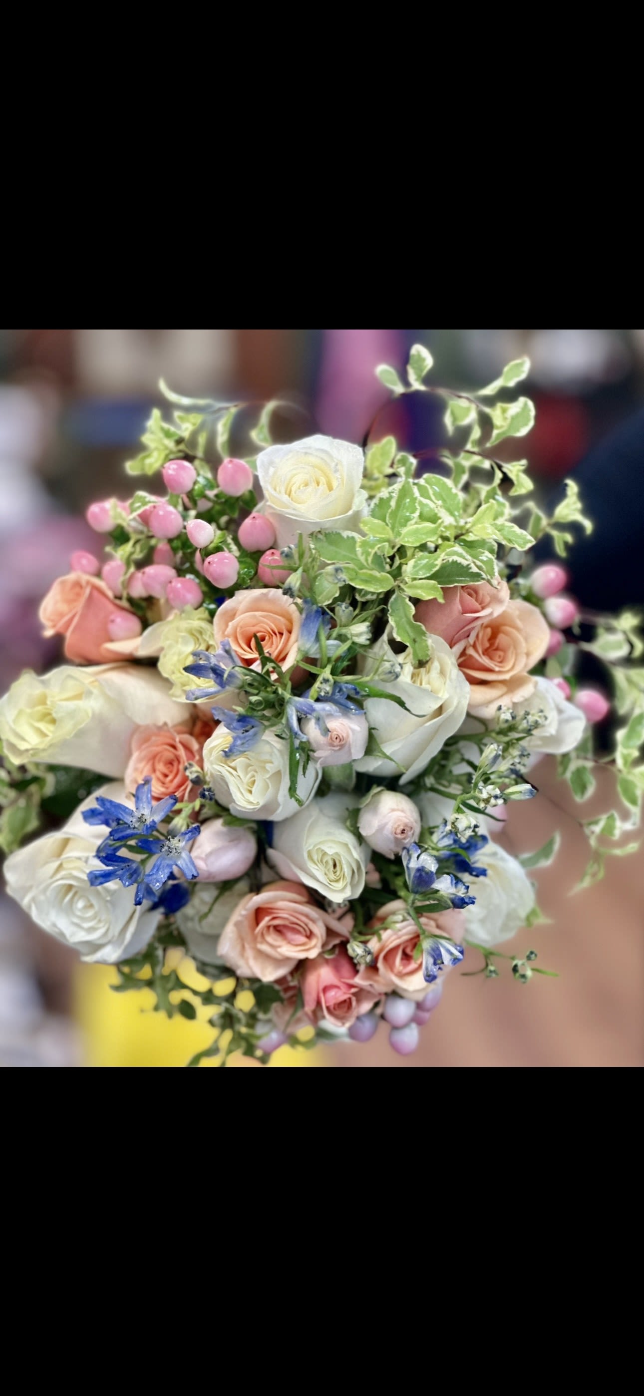 Bouquet of white, blush, and peach roses with blue flowers and pink berries