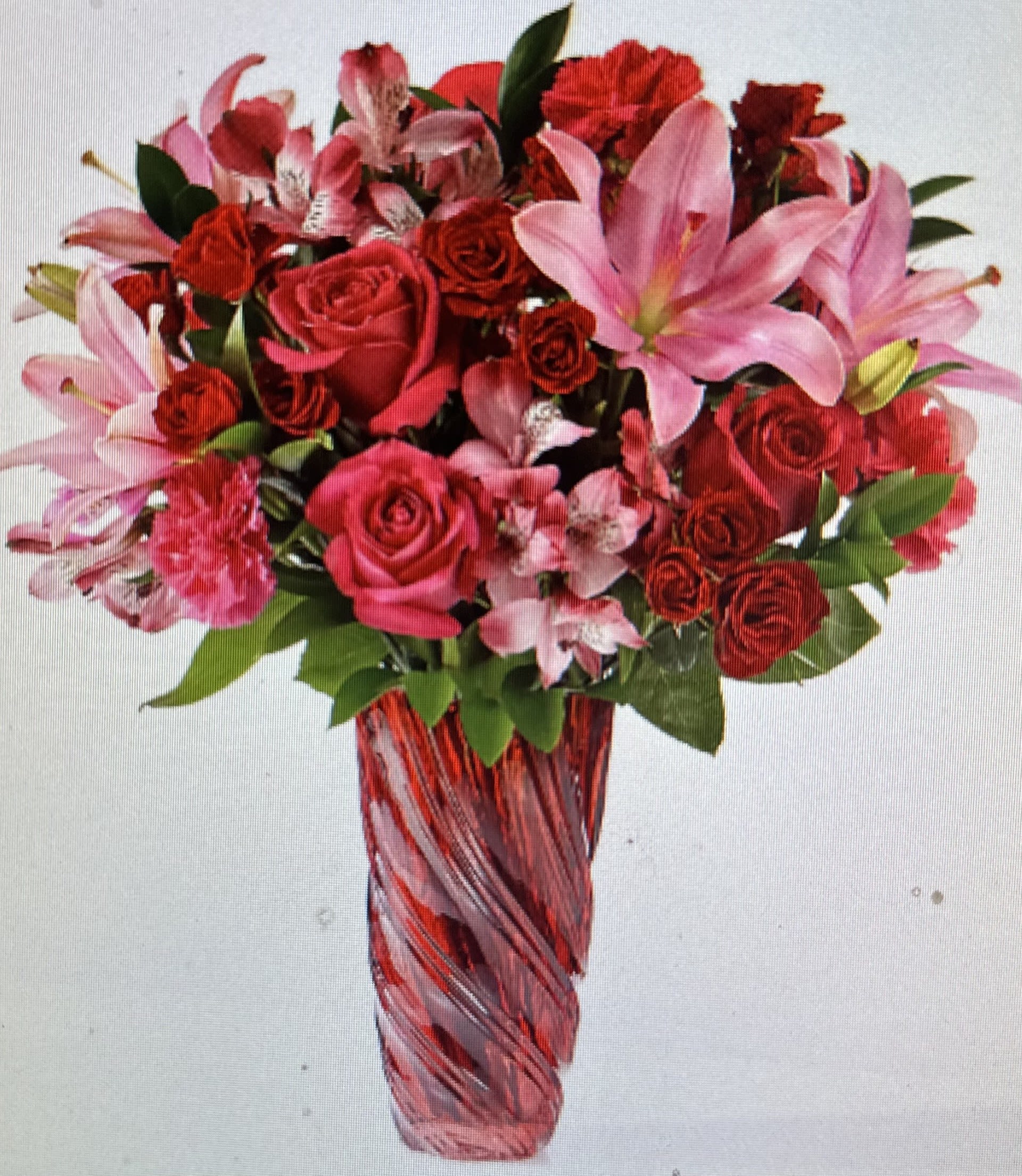 TON O LOVE BOUQUET - STUNNING BOUQUET OF PINK LILIES, ALSTROMERIA, CARNATIONS, ROSES AND SPRAY ROSES IN A VIBRANT RED SWIRLED VASE.