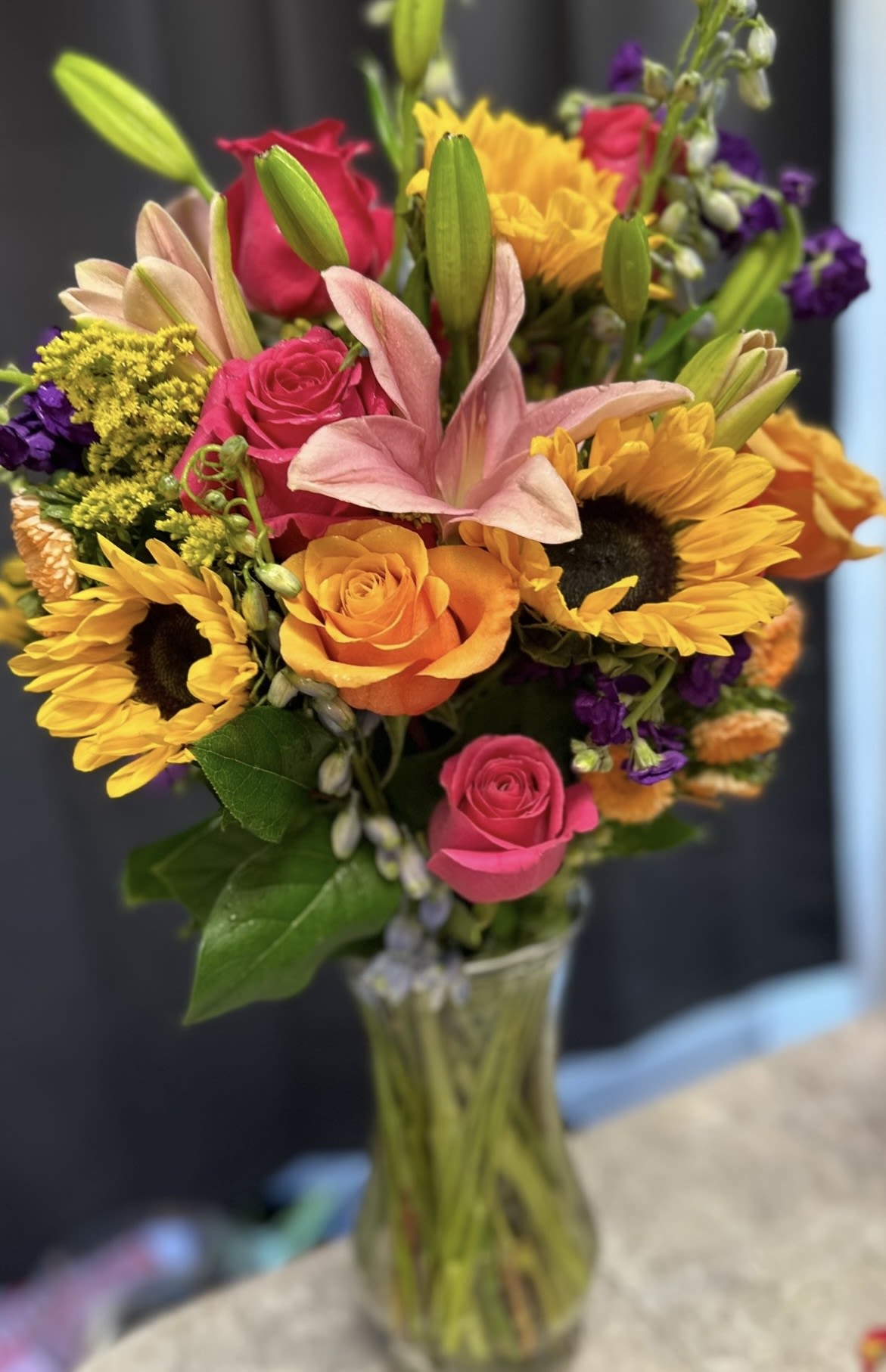 TALL SUNFLOWER SURPRISE - STUNING TALL BOUQUET OF SUNFLOWERS, ROSES, DELPHINIUM, LILIES, ASTERS, AND STOCK IN A CLEAR VASE. A REAL STUNNER