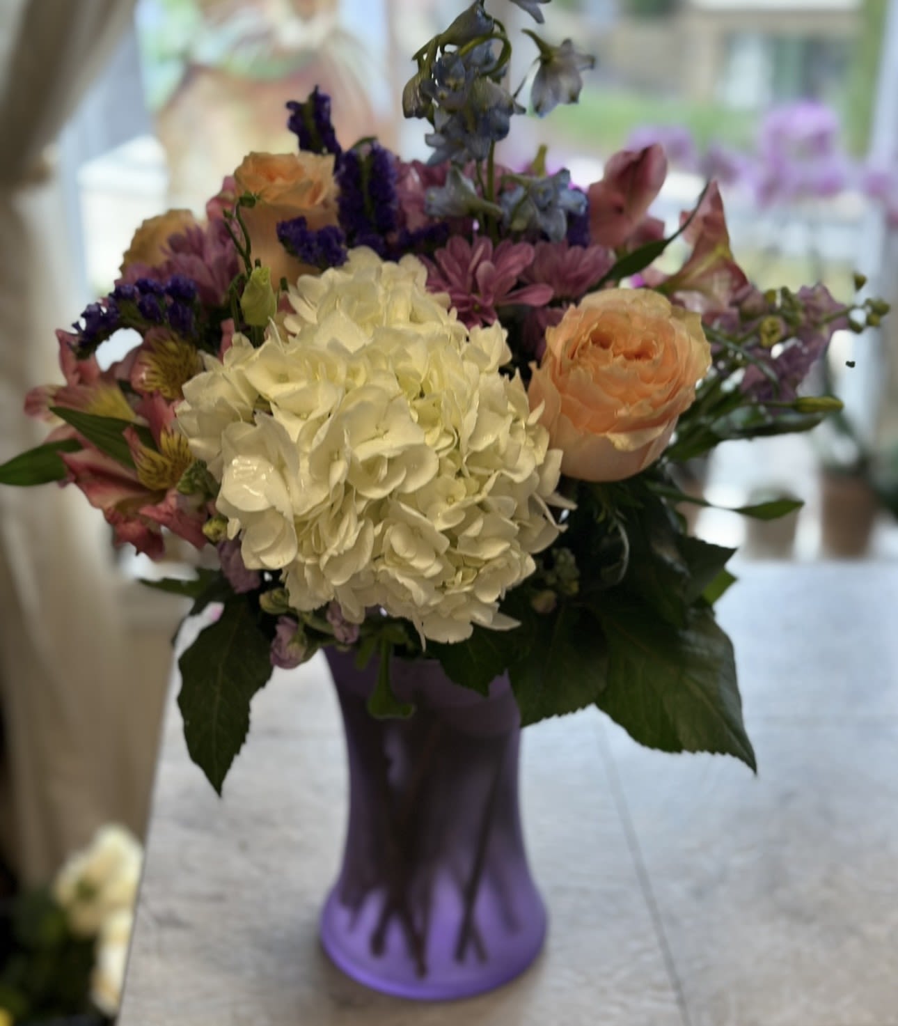 PURPLE PASSION BOUQUET - BEAUTIFUL BOUQUET OF HYDRANGEA, ROSES, DELPHINIUM, STATICE, MUMS, AND ALSTROMERIA IN A BOW WRAPPED PURPLE VASE. VERY FEMININE AND ROMANTIC!