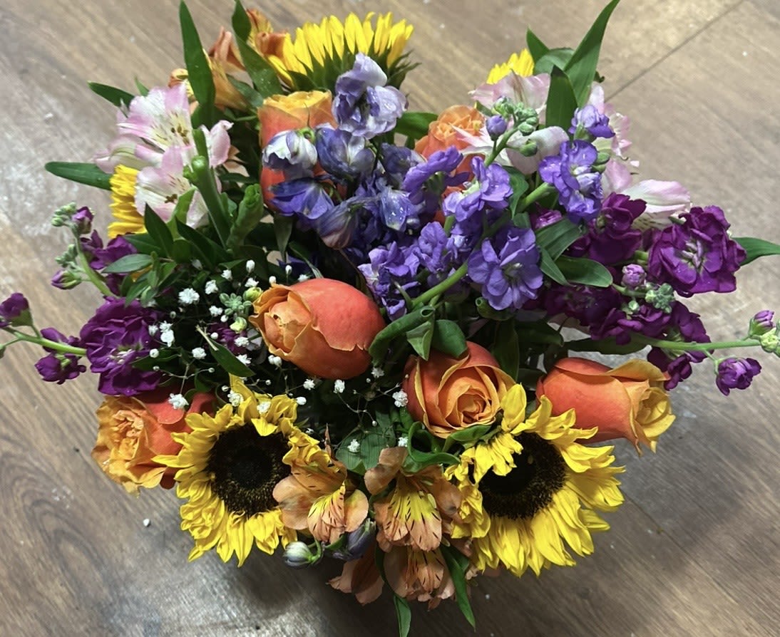 Compact bouquet of yellow sunflowers, orange roses, and purple flowers in a bright mixed arrangement