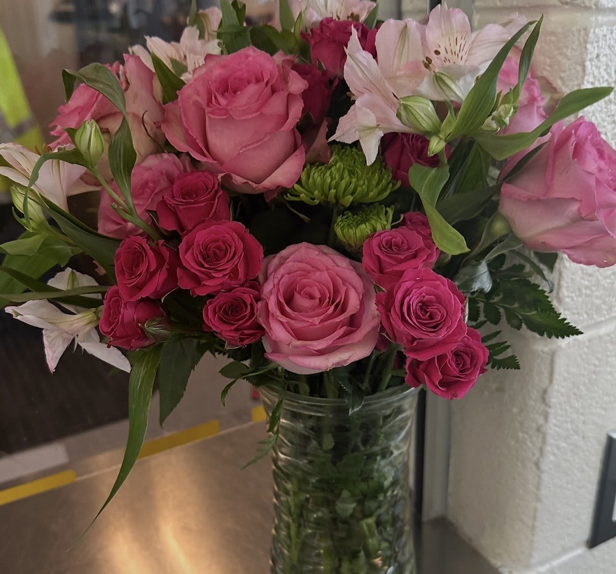Vase arrangement of pink roses, white alstroemeria, and green button mums in a clear glass cylinder