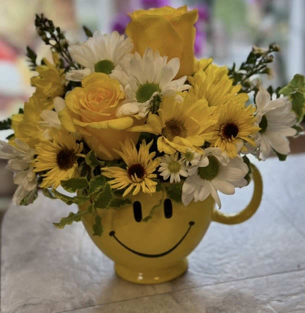 HAPPY HIPPY MUG ARRANGEMENT - FOOD SAFE HAPPY FACED MUG FILLED WITH YELLOW ROSES, WHITE AND YELLOW DAISIES, ASTERS AND GREENS. SURE TO BRING A SMILE!!