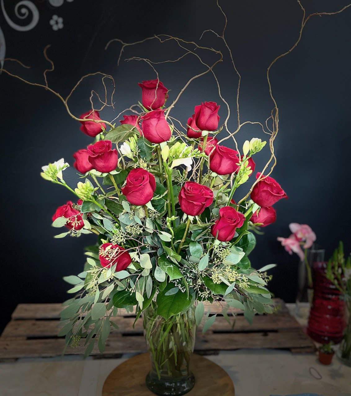Tall bouquet of red roses in a glass vase with curly branches