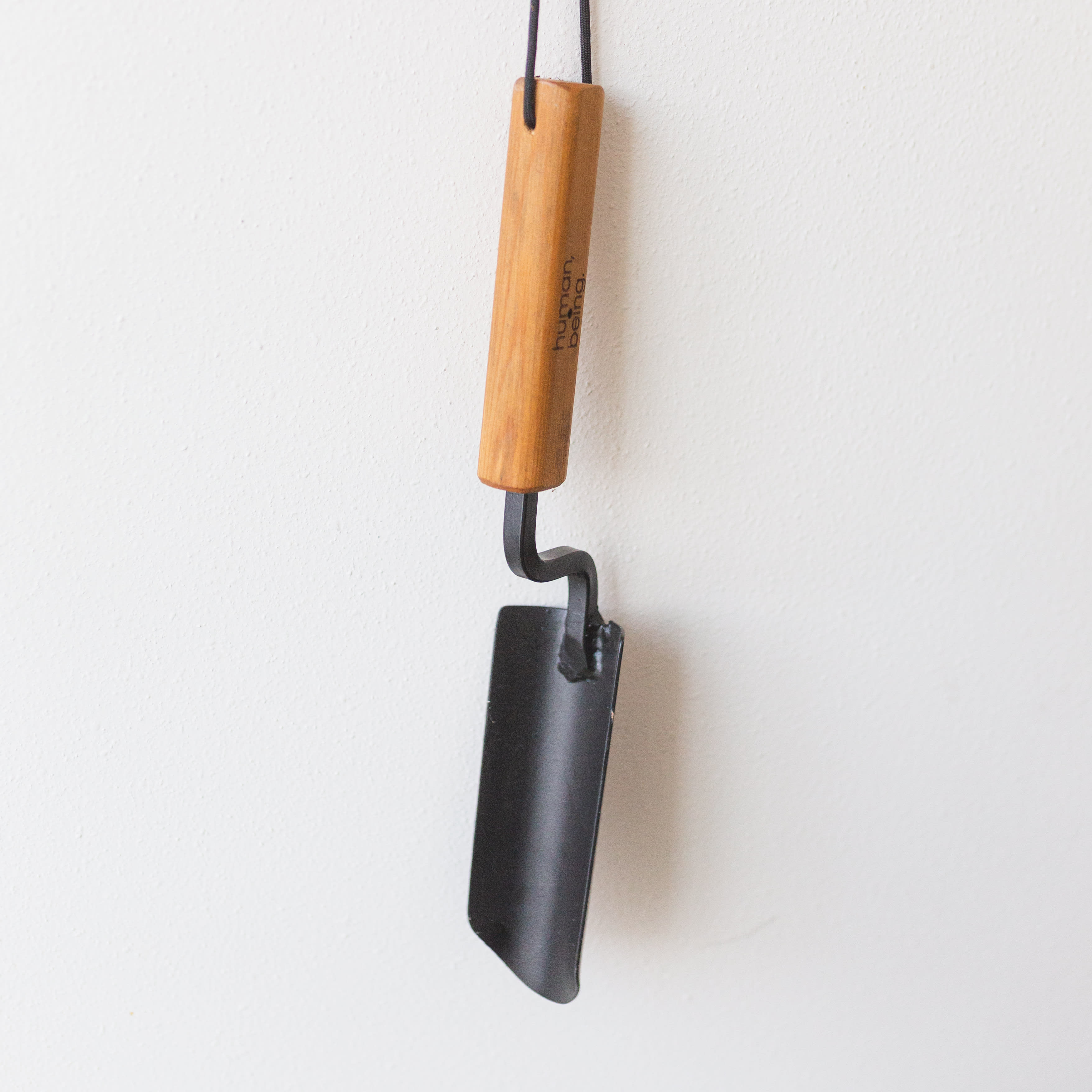 A hanging metal tool with a wooden handle against a white wall.