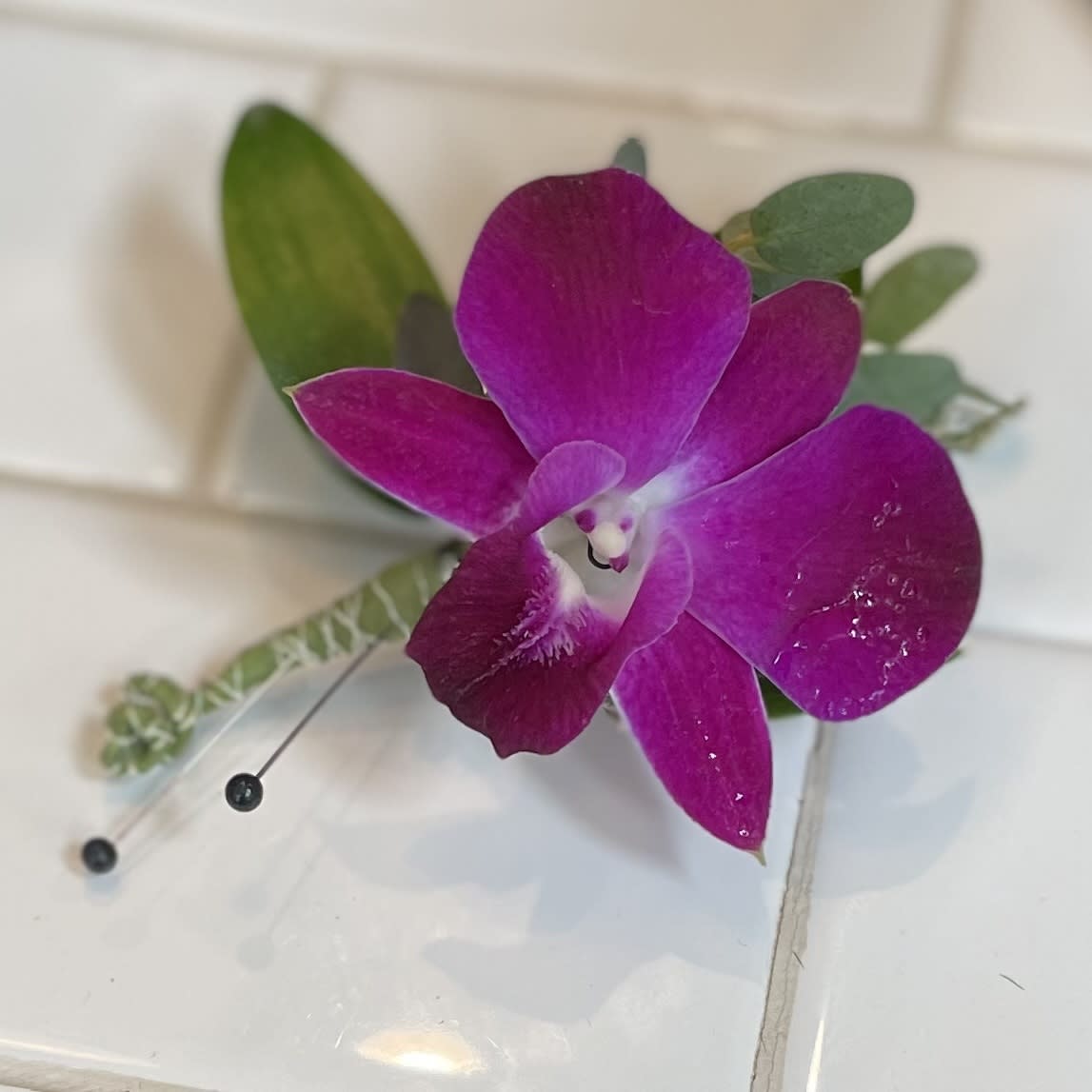 Purple orchid boutonniere with green leaves and pins