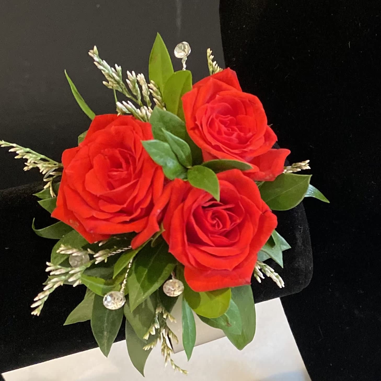 Red rose boutonniere with green leaves and small white accents