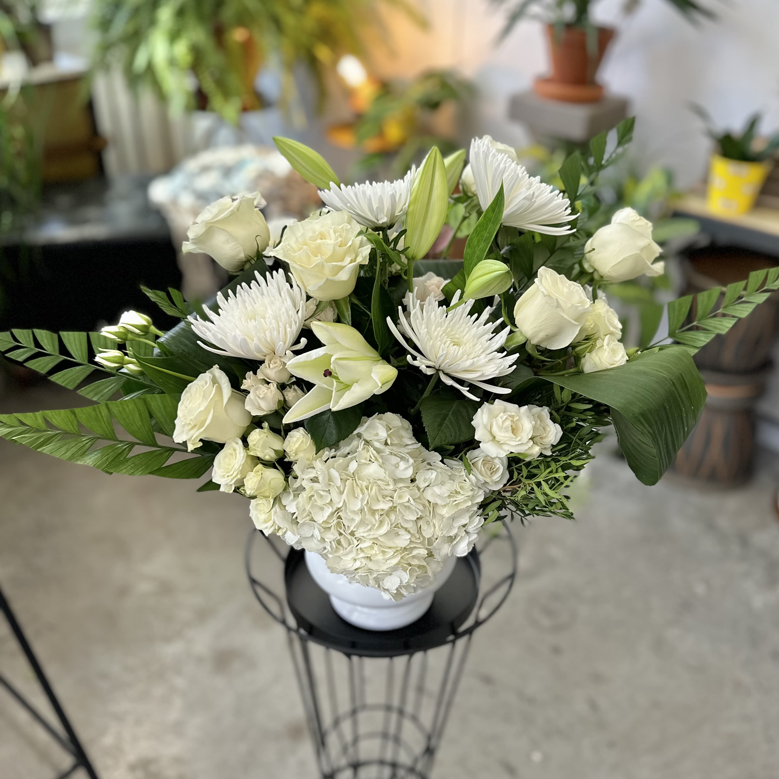 White floral arrangement in a white vase with lilies, roses, and chrysanthemums