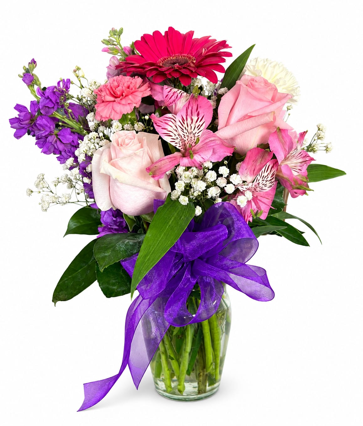 Mixed bouquet of pink, purple, and white flowers in a glass vase with a purple ribbon