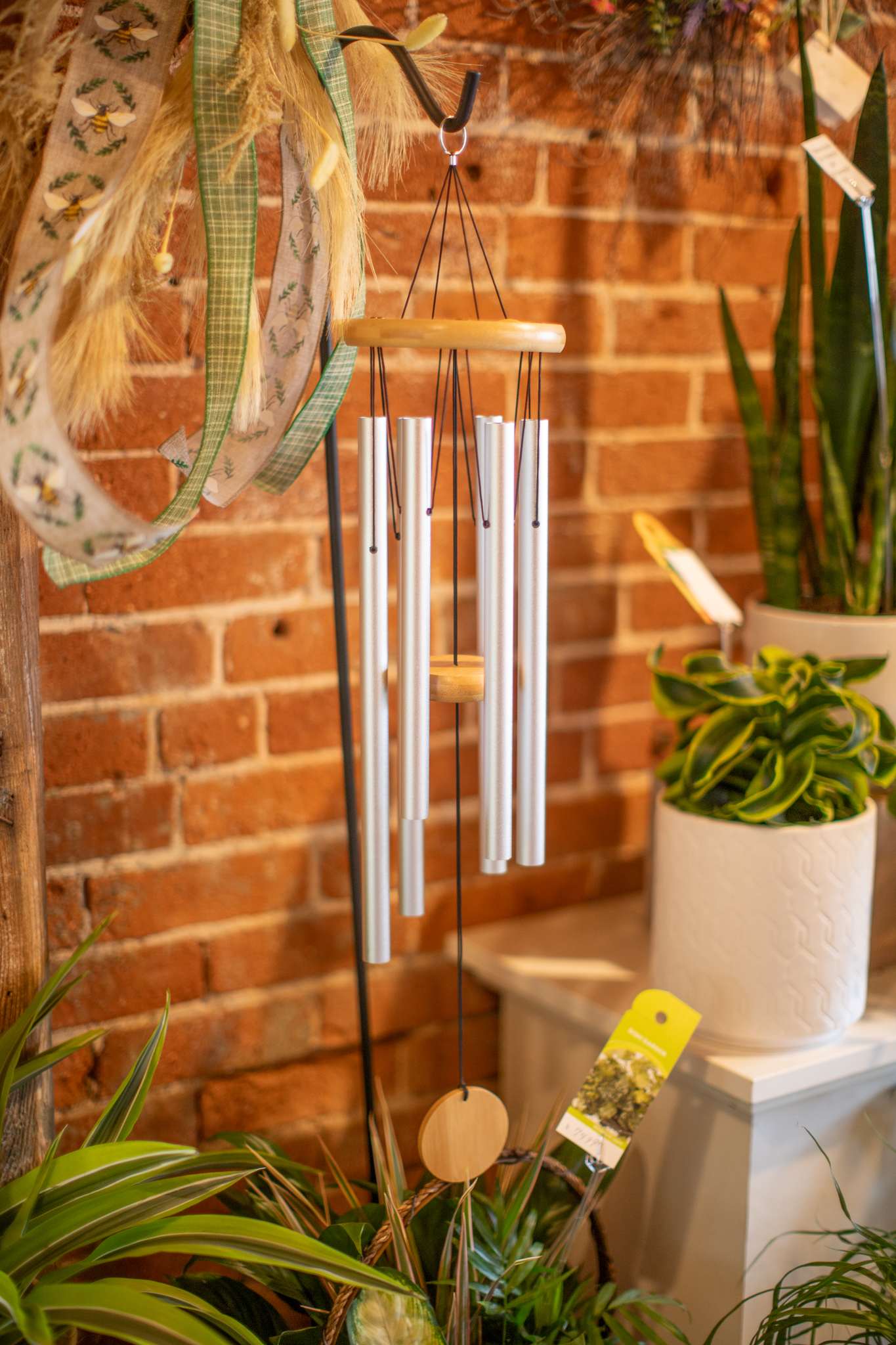 Silver wind chime hanging in front of a brick wall with potted plants nearby