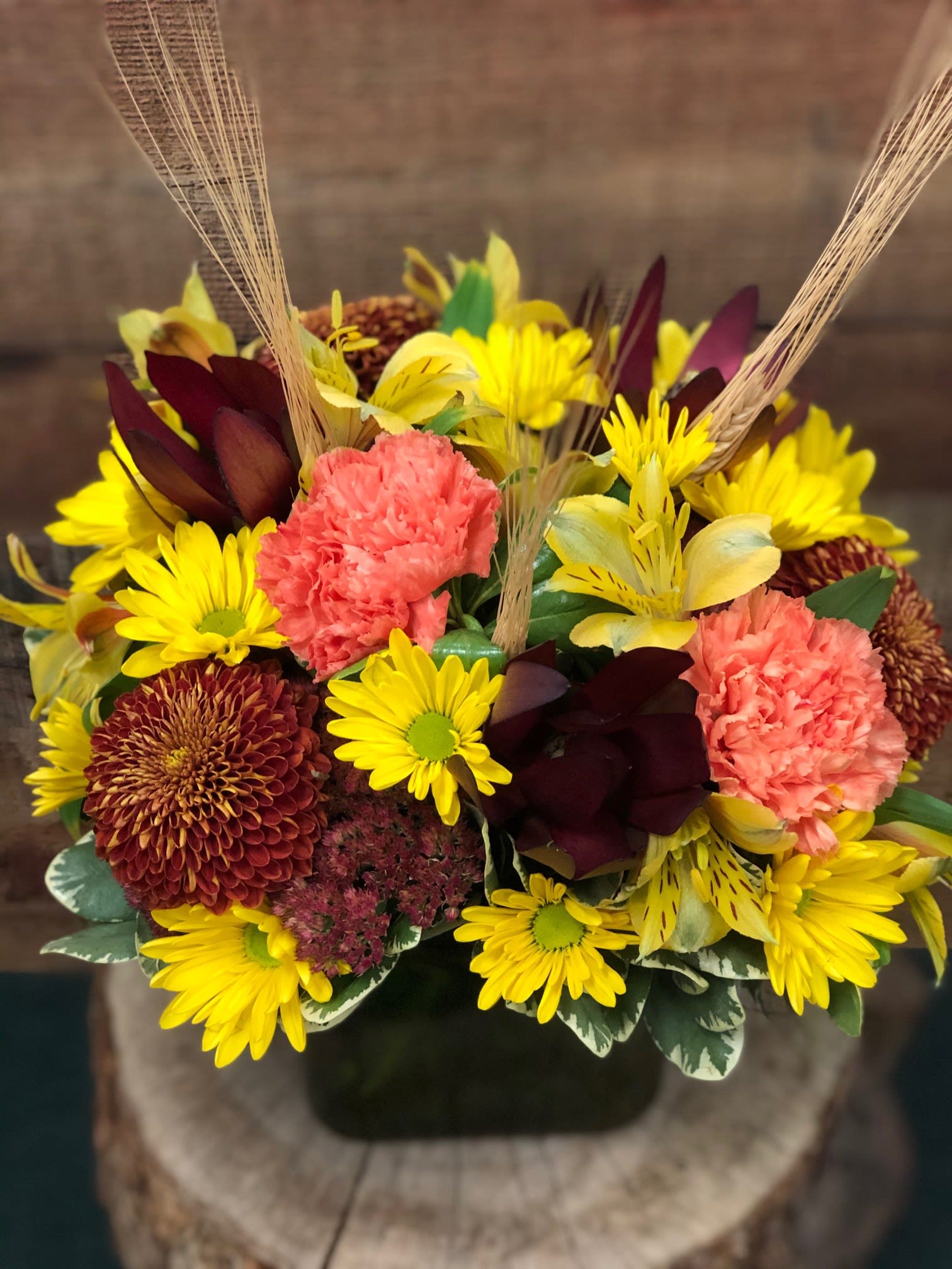Fall Fantasy - A beautiful display of traditional autumn colors designed with long lasting flowers. Brilliant oranges and vibrant yellows accented with a splash of dried wheat nestled into a modern cube vase. 