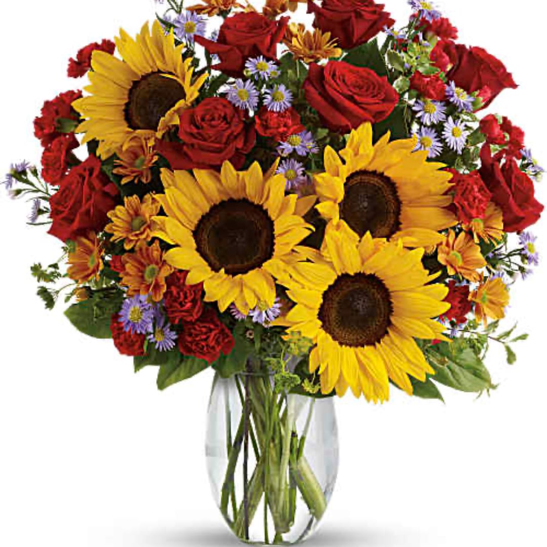 Bouquet of sunflowers, red roses, and small purple daisies in a clear glass vase