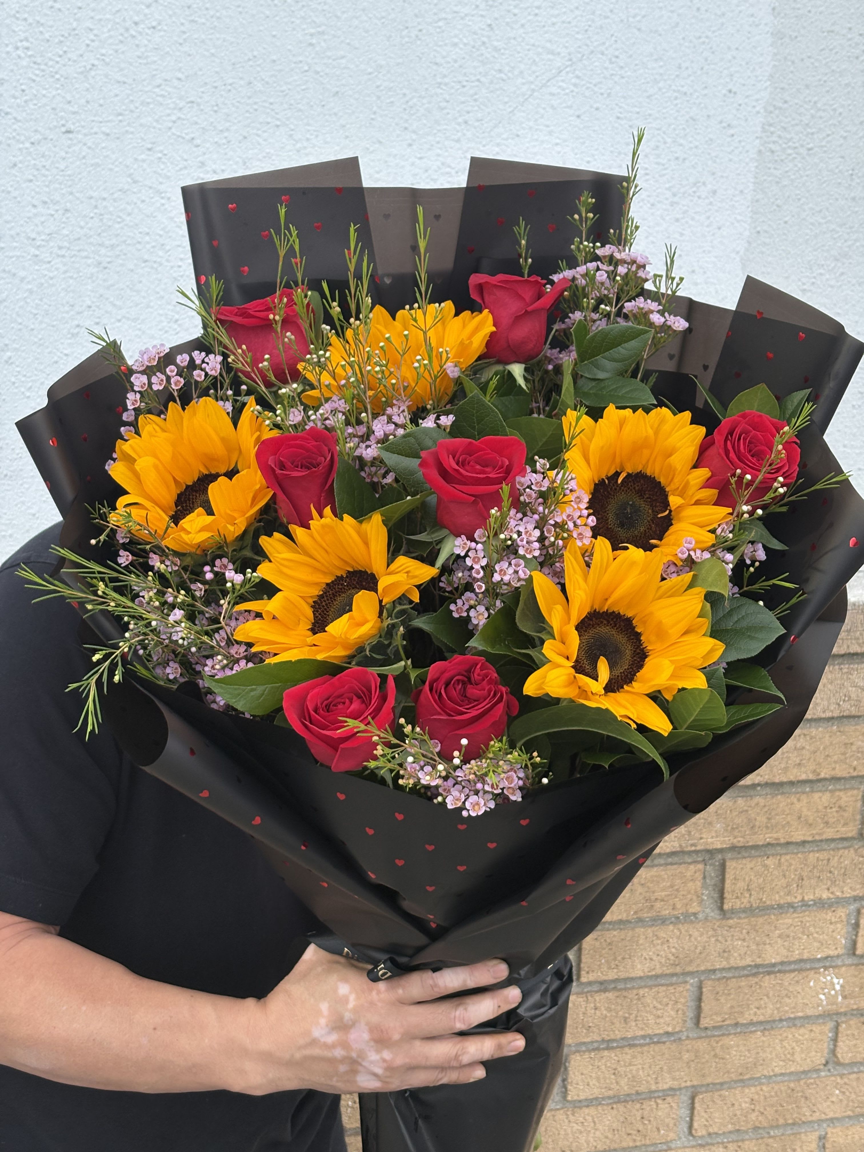 Bouquet of red roses and sunflowers wrapped in black paper
