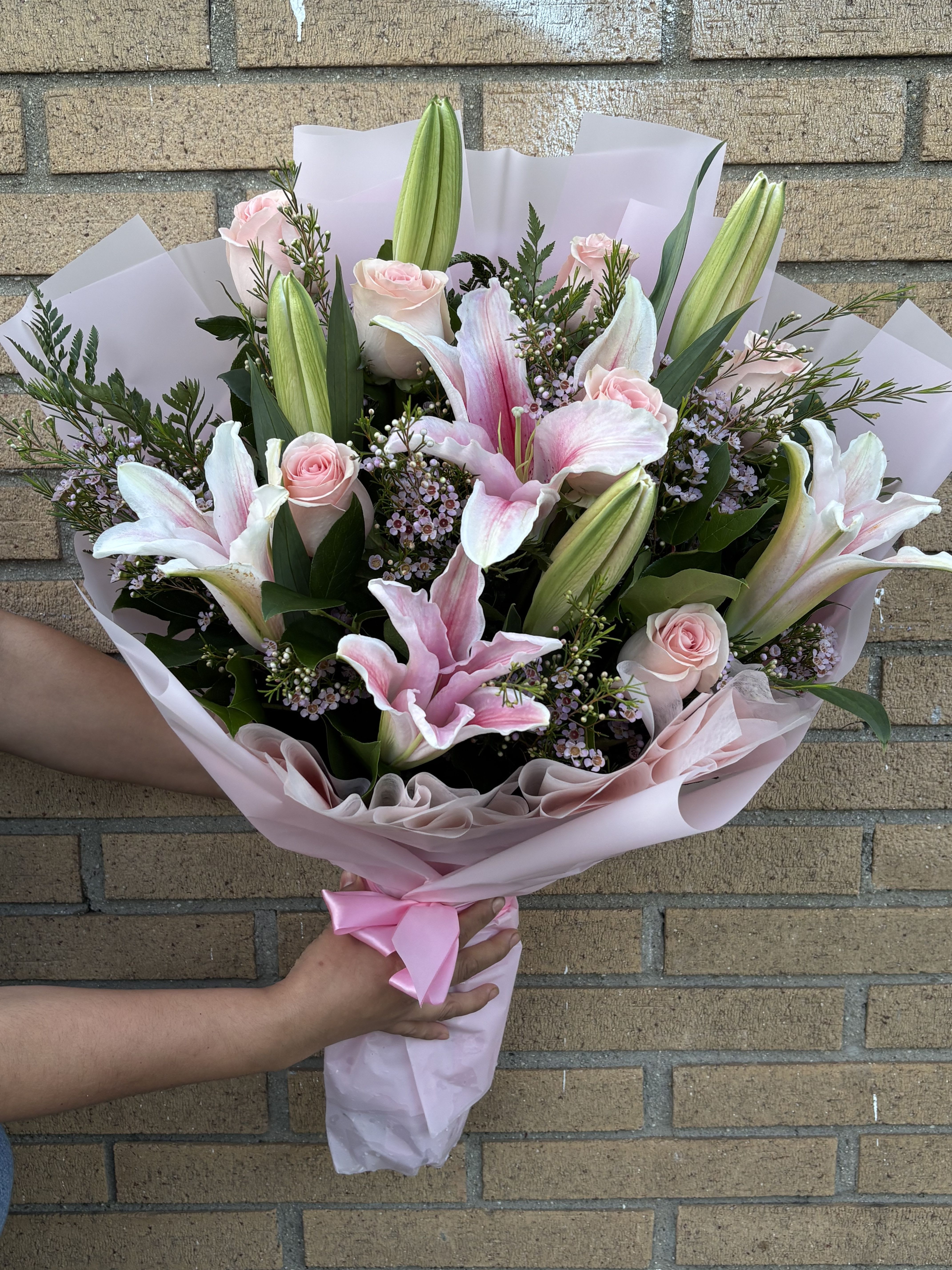 Pink roses and lilies in a wrapped bouquet with a satin ribbon