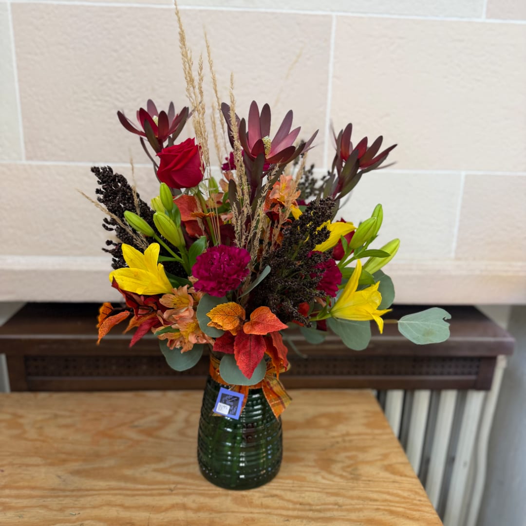Autumn bouquet with red roses, yellow lilies, and a green glass vase