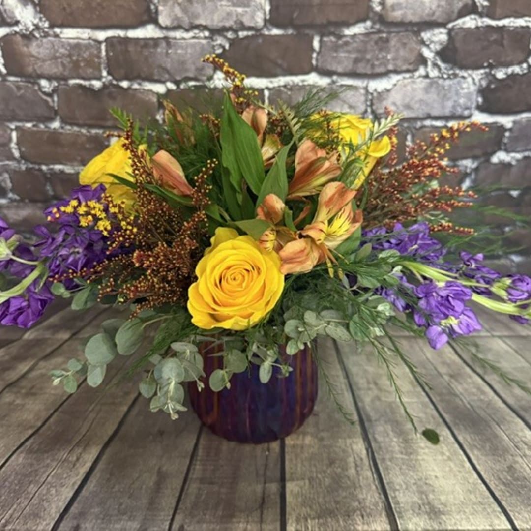Yellow rose and purple flower arrangement in a dark glass vase
