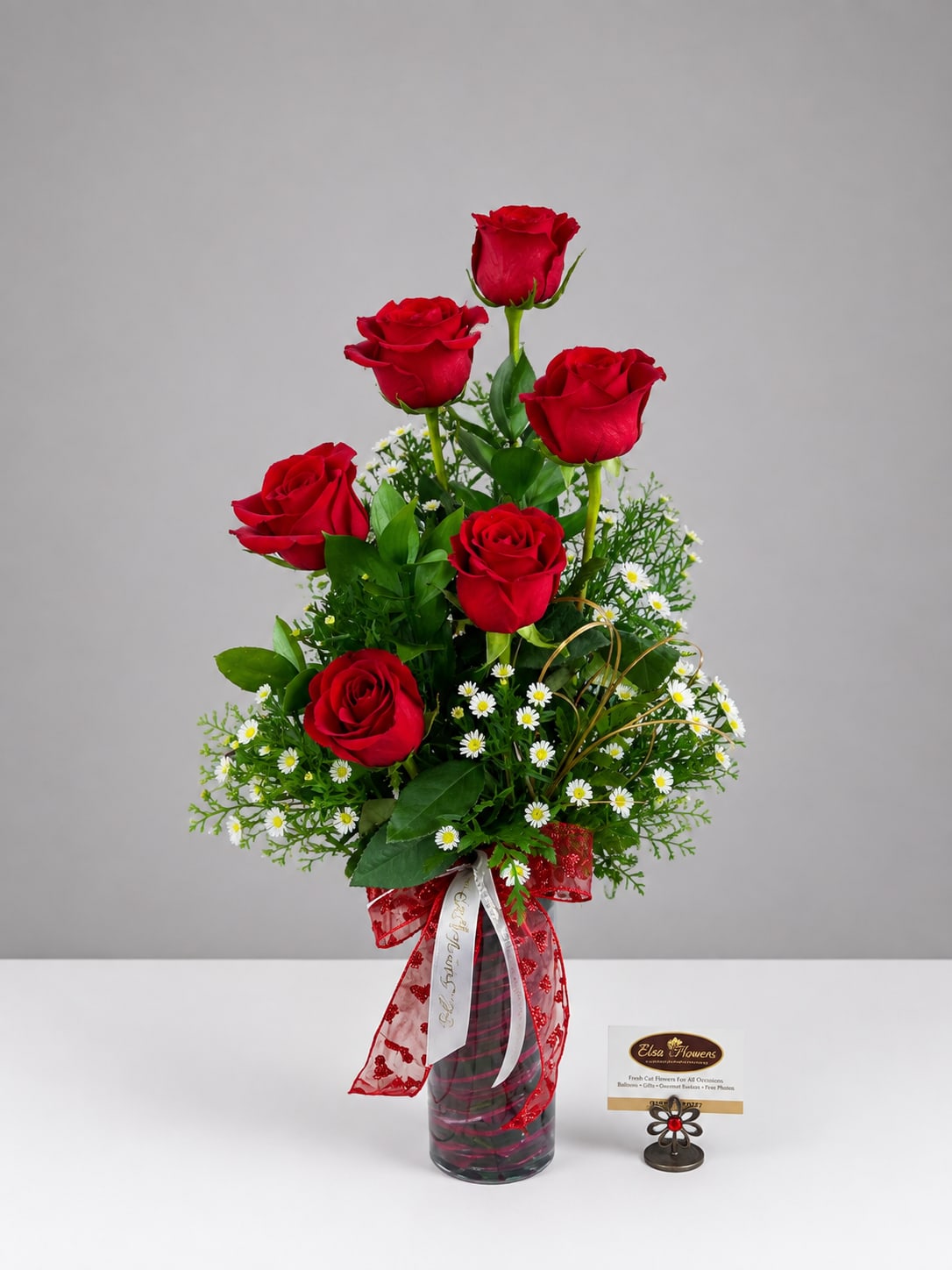 Red roses arranged in a glass vase with small white daisies