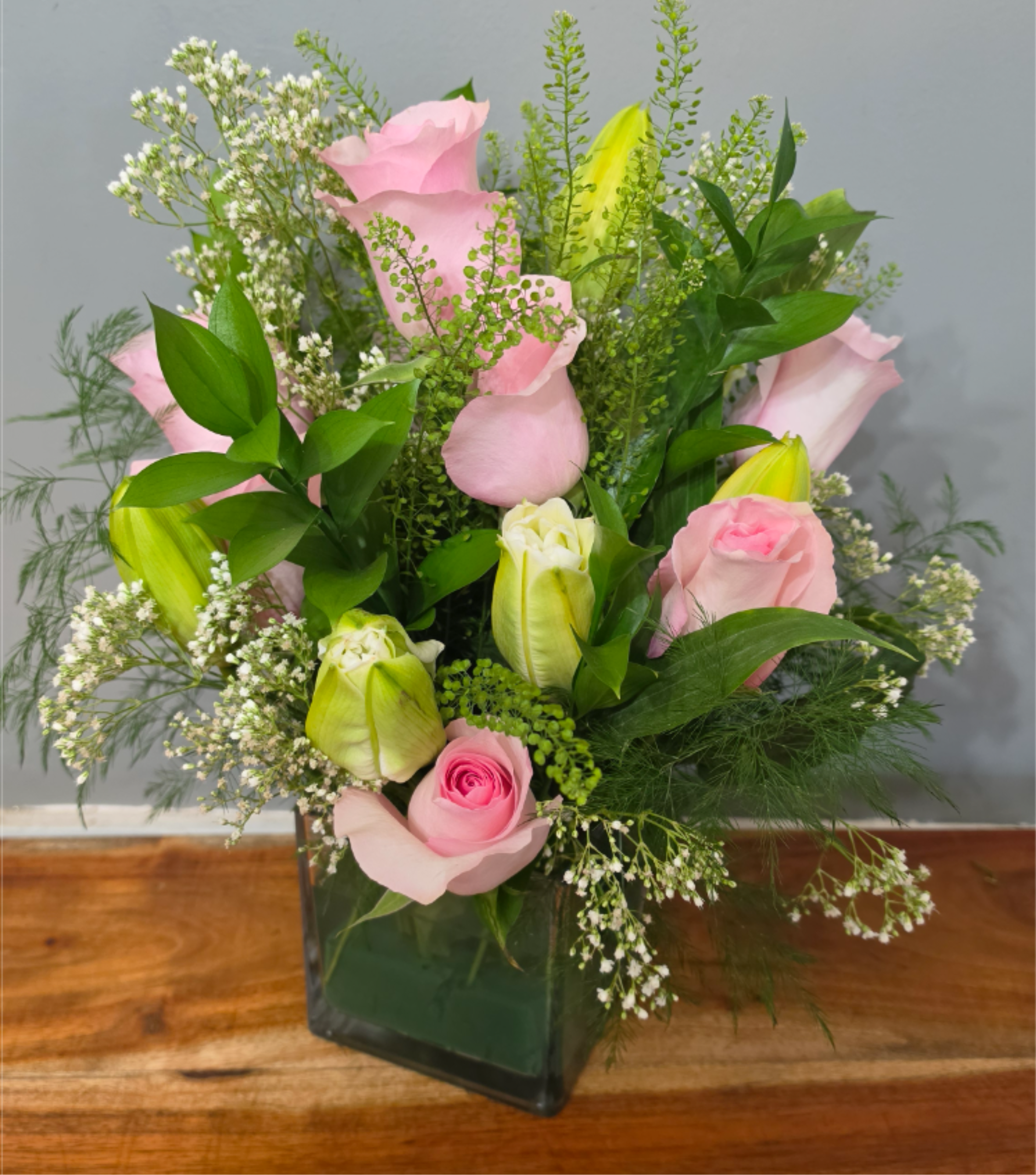 Pink  Princess  - A pastel garden that reads like a gentle embrace, Pink Princess is a birthday bouquet and thinking-of-you arrangement that makes the person you're sending it to feel seen and comforted. Soft pink roses sit alongside white lilies to create a romantic-yet-casual mood perfect for birthdays, a quiet anniversary surprise, or a thoughtful Mother's Day gift for the mom who prefers understated elegance.  Arranged upright in a clear square glass vase, the design is loose and layered with airy white filler, branching accents, and textured greenery for a fresh, garden-picked silhouette. You'll notice roses, ranunculus, lilies, and tulips in shades of pink, white, and green (with a touch of yellow visible in photos), arranged to sit compactly in the cube vase so it fits neatly on a table, desk, or bedside. The pastel palette keeps the look bright and lively while remaining tender and hopeful.  Send Pink Princess to mark a birthday, say "I'm thinking of you," or celebrate an anniversary with something quietly romantic; it's an elegant everyday size that still feels special. Care is simple-keep water fresh and trim stems every few days-to help these tender blooms last. Available for delivery in West Frankfort, IL.
