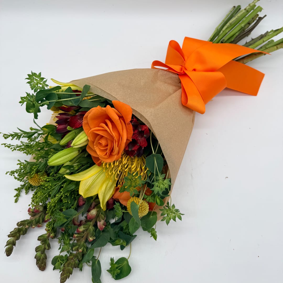 Bouquet of orange and yellow flowers wrapped in brown paper with an orange ribbon