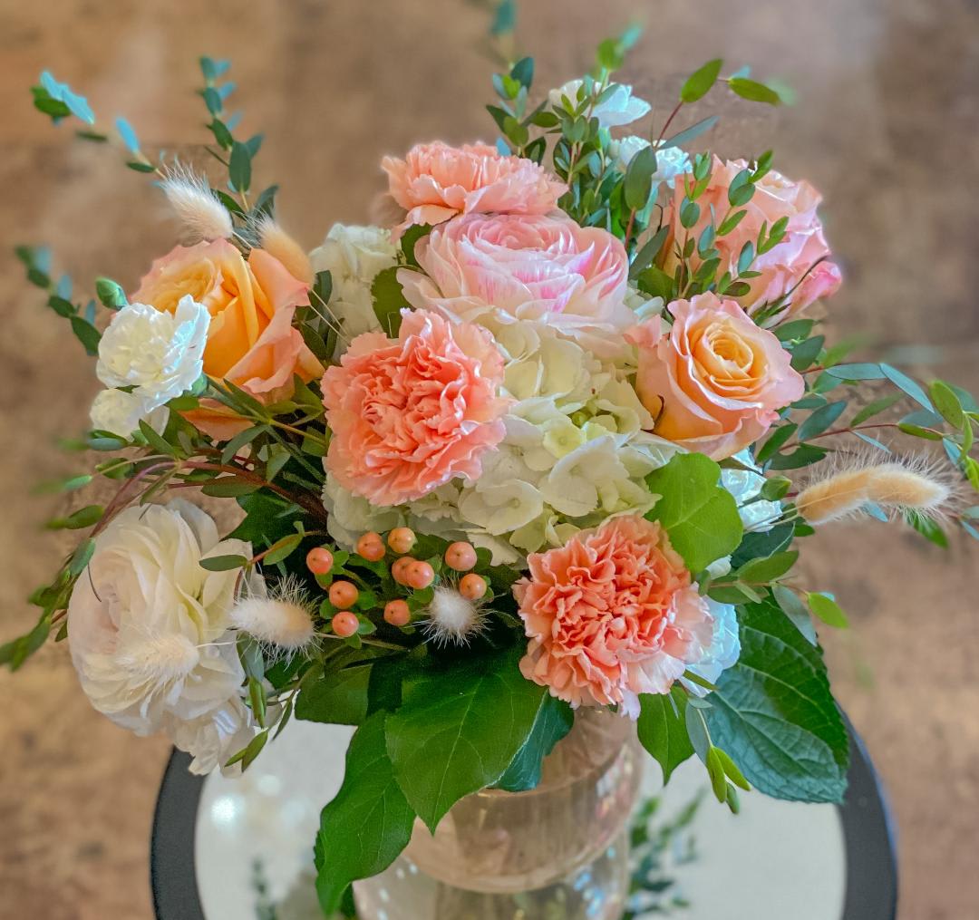 Peach and white bouquet with roses, carnations, and hydrangea in a glass vase