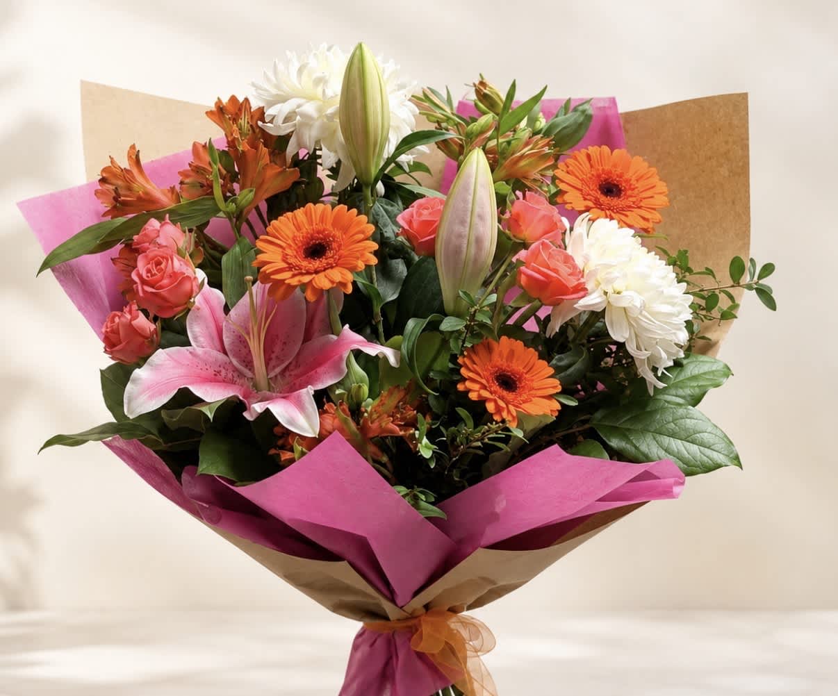 Bouquet of pink lilies, orange gerberas, roses, and white chrysanthemums wrapped in pink paper