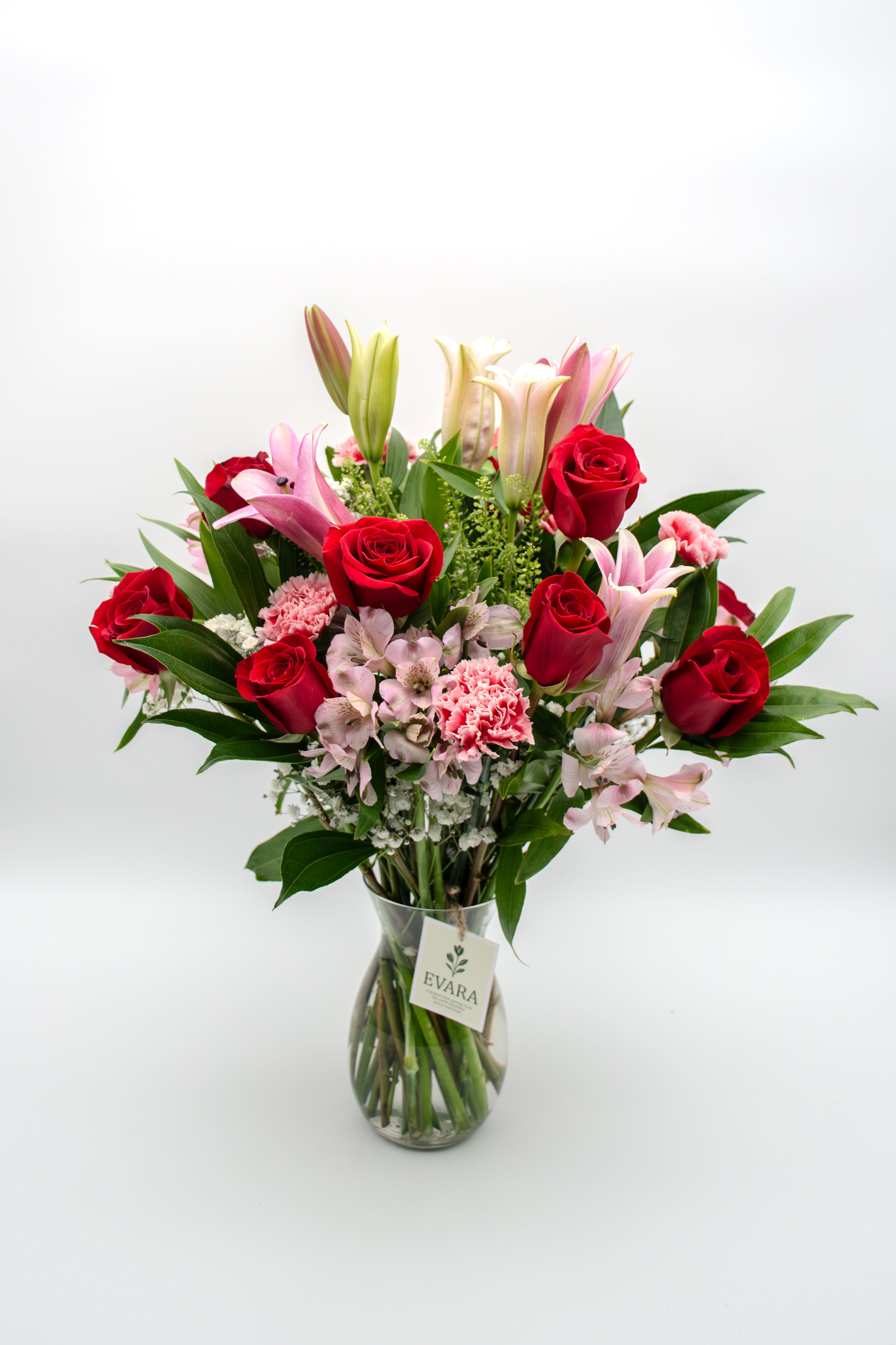 Bouquet of red roses, pink lilies, and carnations in a glass vase