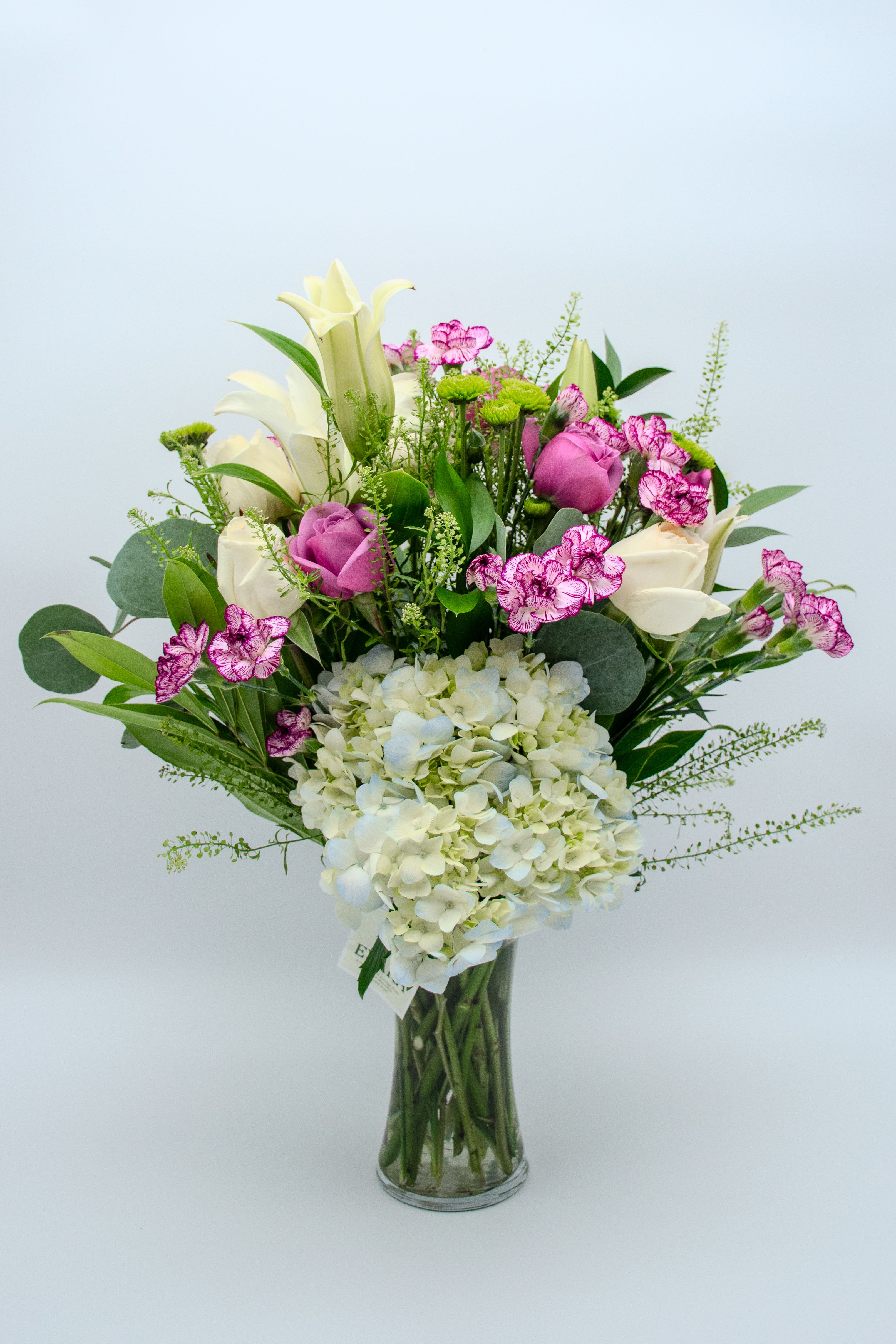 Bouquet of white lilies, pink roses, and hydrangea in a glass vase