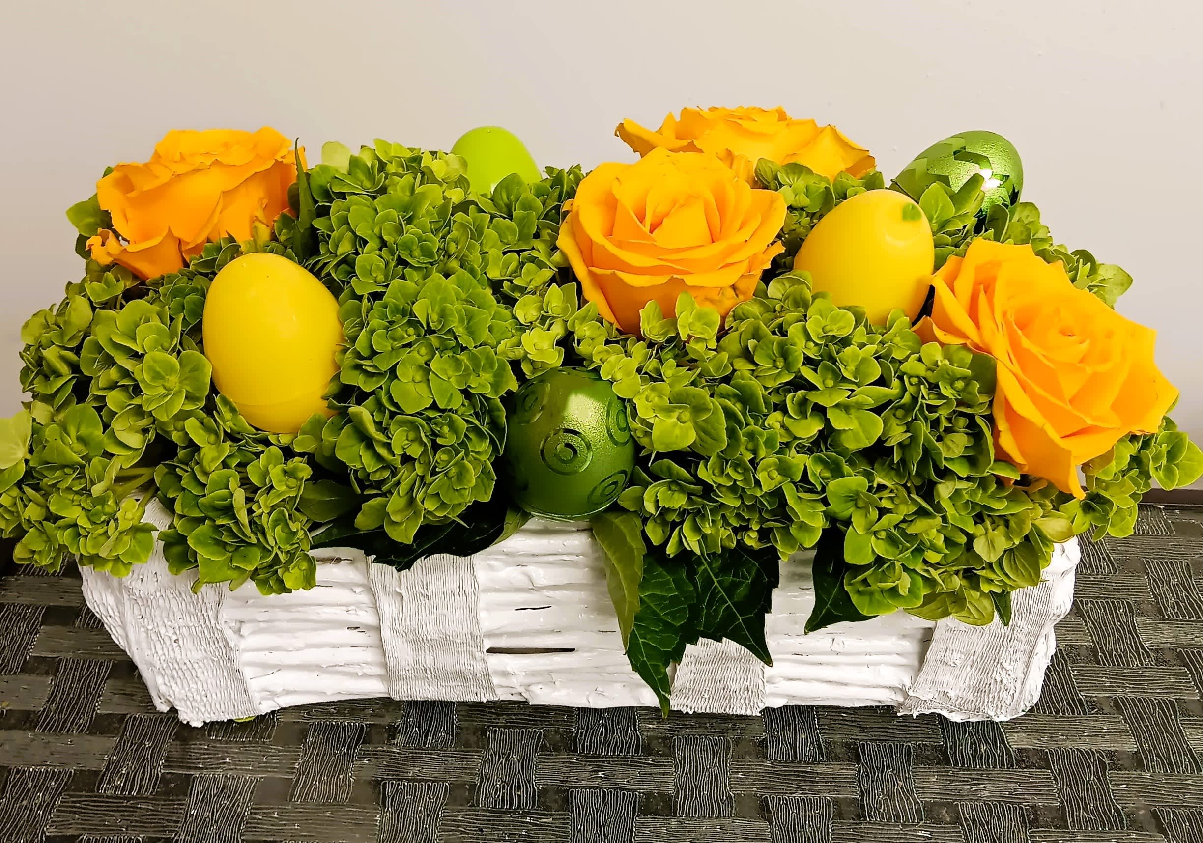 Yellow roses and green hydrangeas in a white basket with decorative eggs